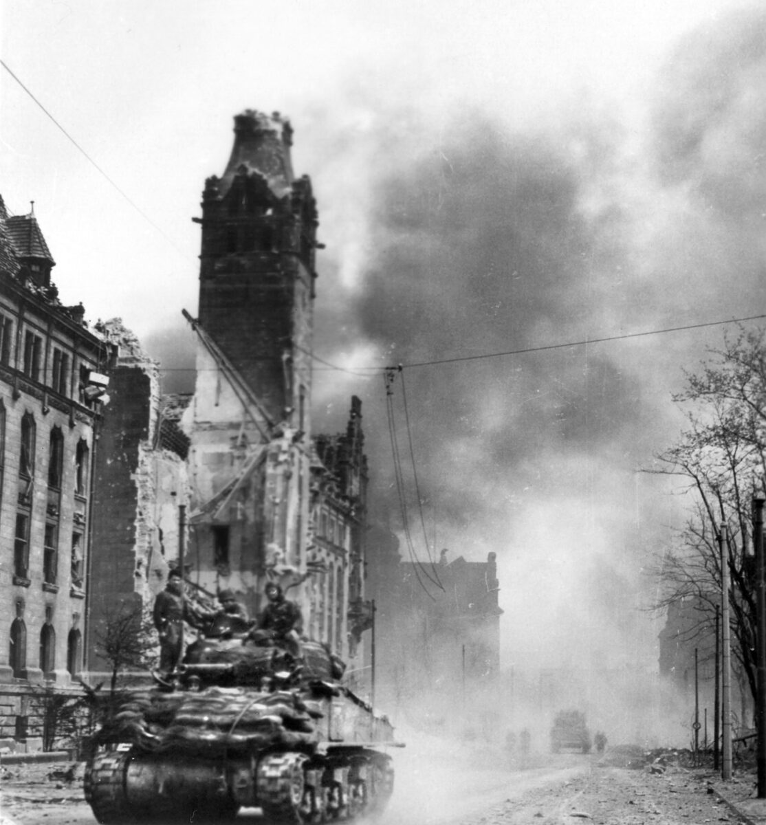 A Sherman tank of the 2nd Armored Division rolls through a burning German city. The towns and cities in the path of the advance suffered heavy damage when the enemy chose to stand and fight. 
