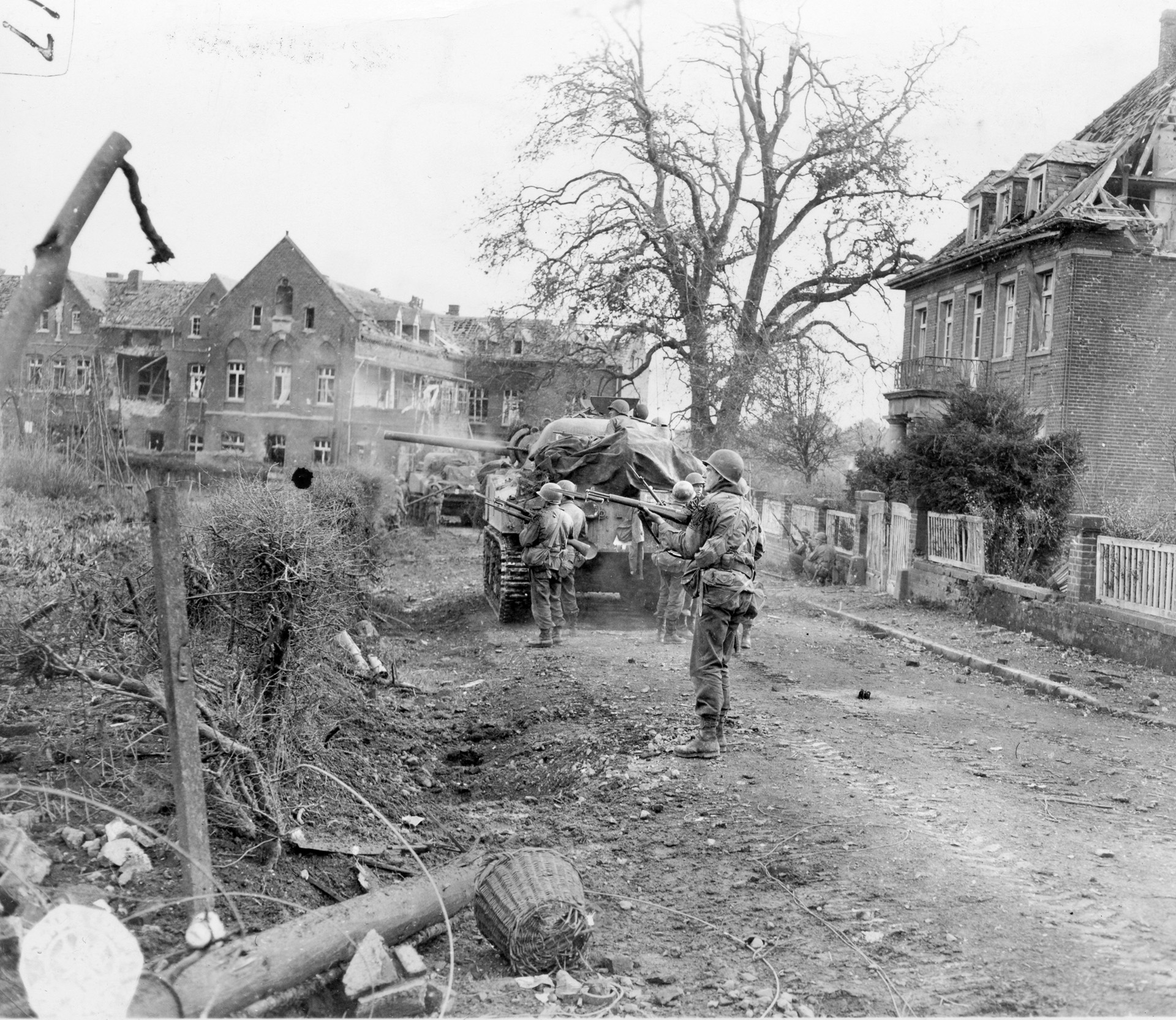 Soldiers of the 333rd Regiment, 84th Infantry Division (“Railsplitters”), advance behind an M4A3 Sherman tank as it uses its hull-mounted machine gun to blast an enemy position in a residential section of Geilenkirchen, Germany.