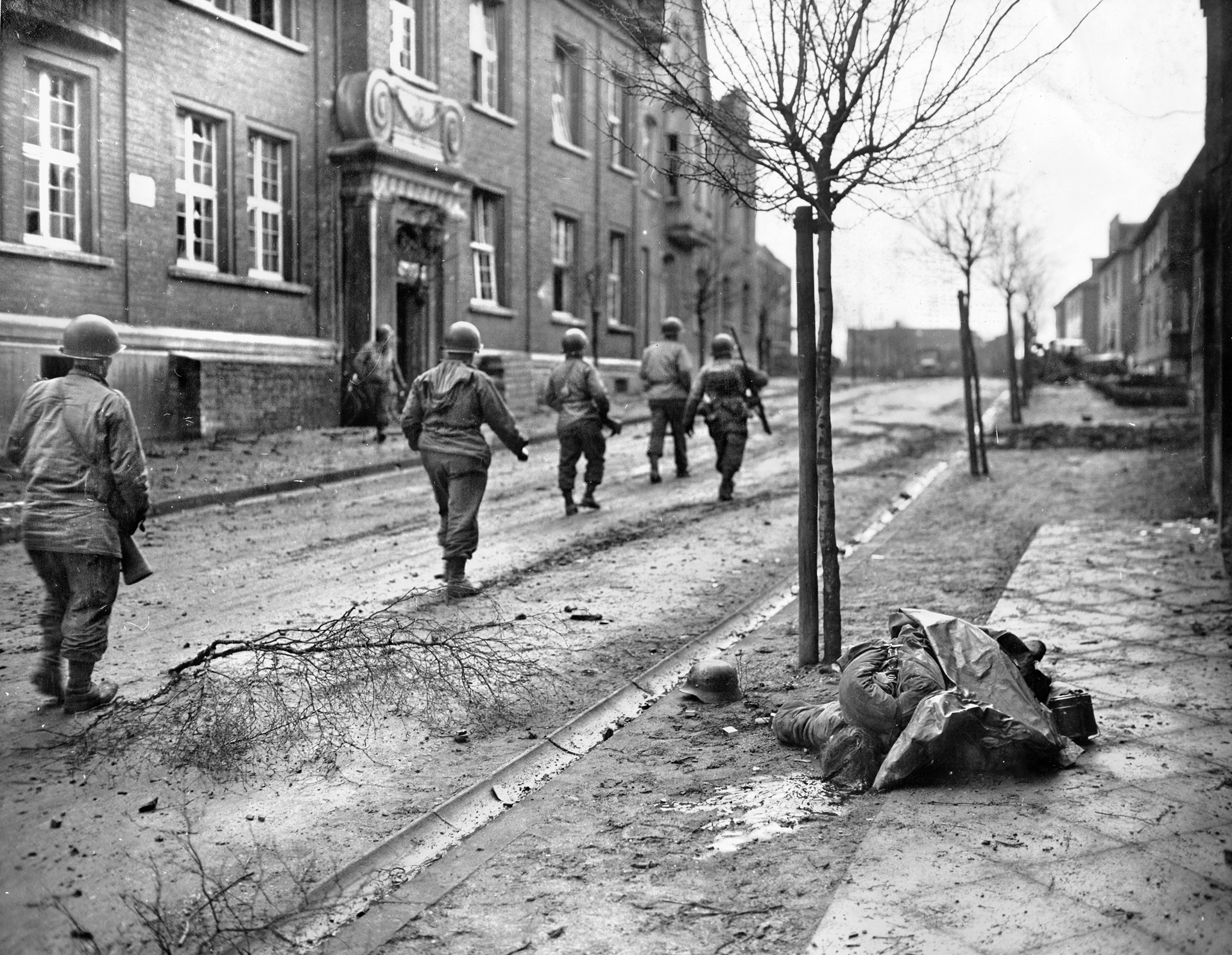 Men of the 320th Infantry Regiment, 35th Infantry Division, Ninth Army, file past the corpse of a German soldier in the German town of Kamp-Lintfort, west of Essen. 