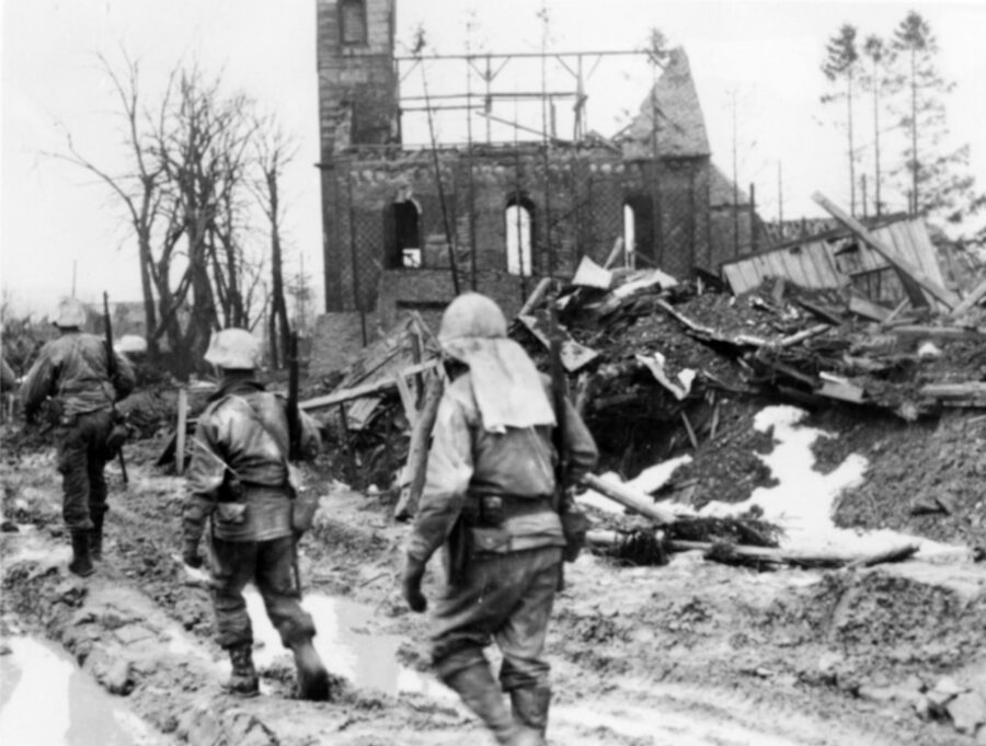 With their helmets painted white to blend with the patchy February snow, men of the 2nd Infantry Division move past a ruined church in Harperschied, Germany. 