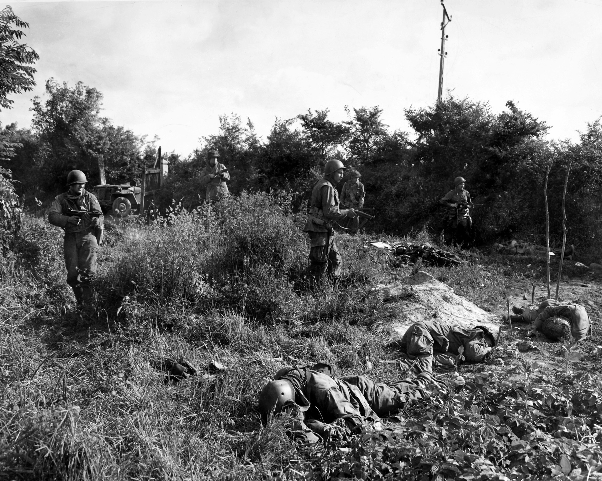 American paratroopers, with their weapons at the ready, advance cautiously through a field near Carentan littered with the bodies of their comrades, picked off by German sharpshooters, June 14, 1944.