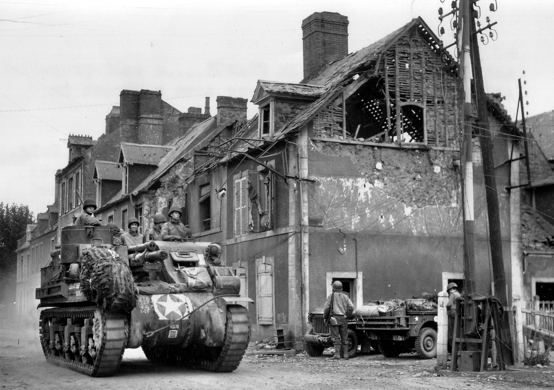 With Carentan secured, an M7 “Priest” self-propelled gun of the 14th Armored Field Artillery Battalion, 2nd Armored Division, rolls through the intersection of Holgate Street near the train station on June 18, 1944. 