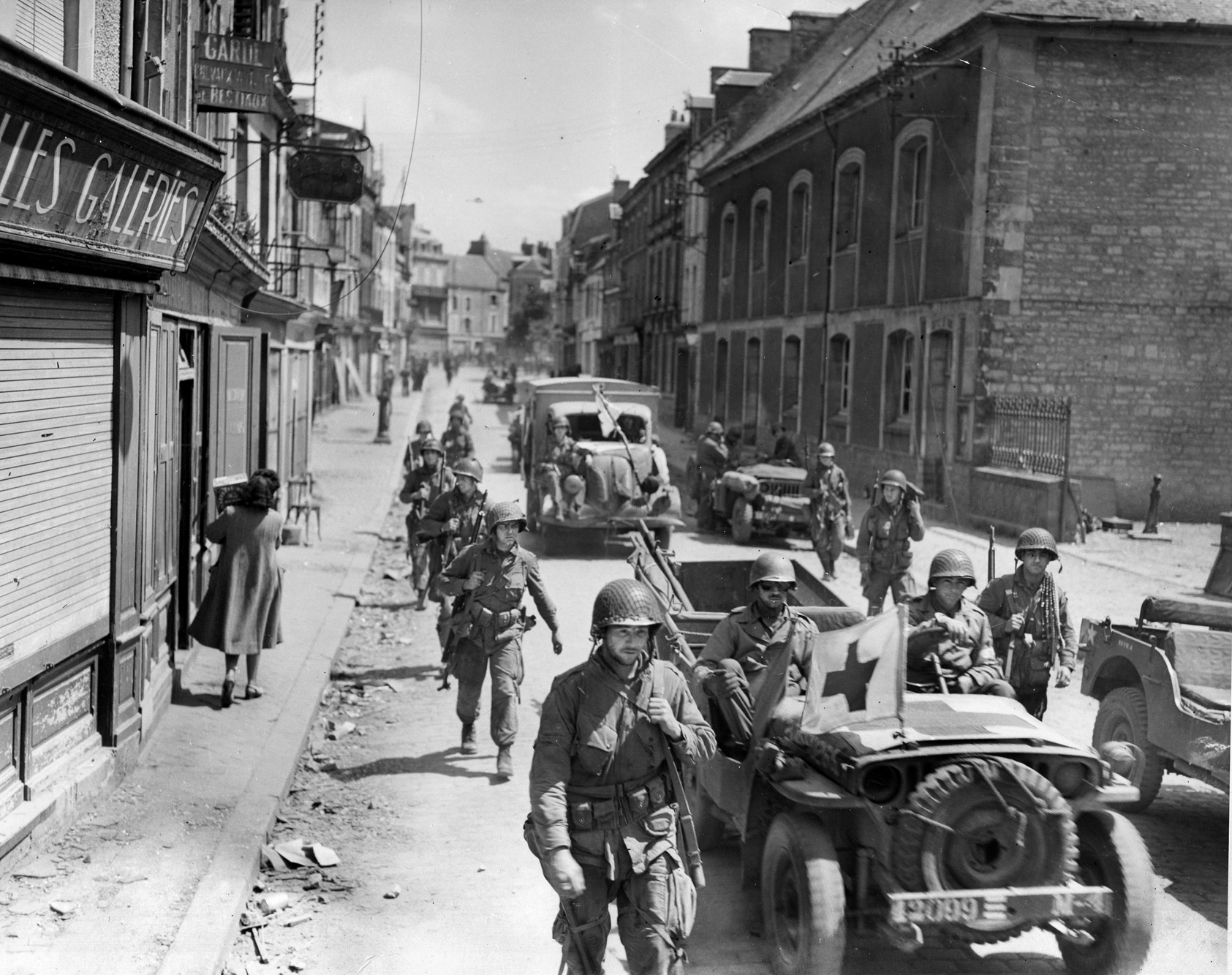 Stiff enemy opposition having finally been overcome, troops and vehicles, including a medical jeep, roll through Carentan.