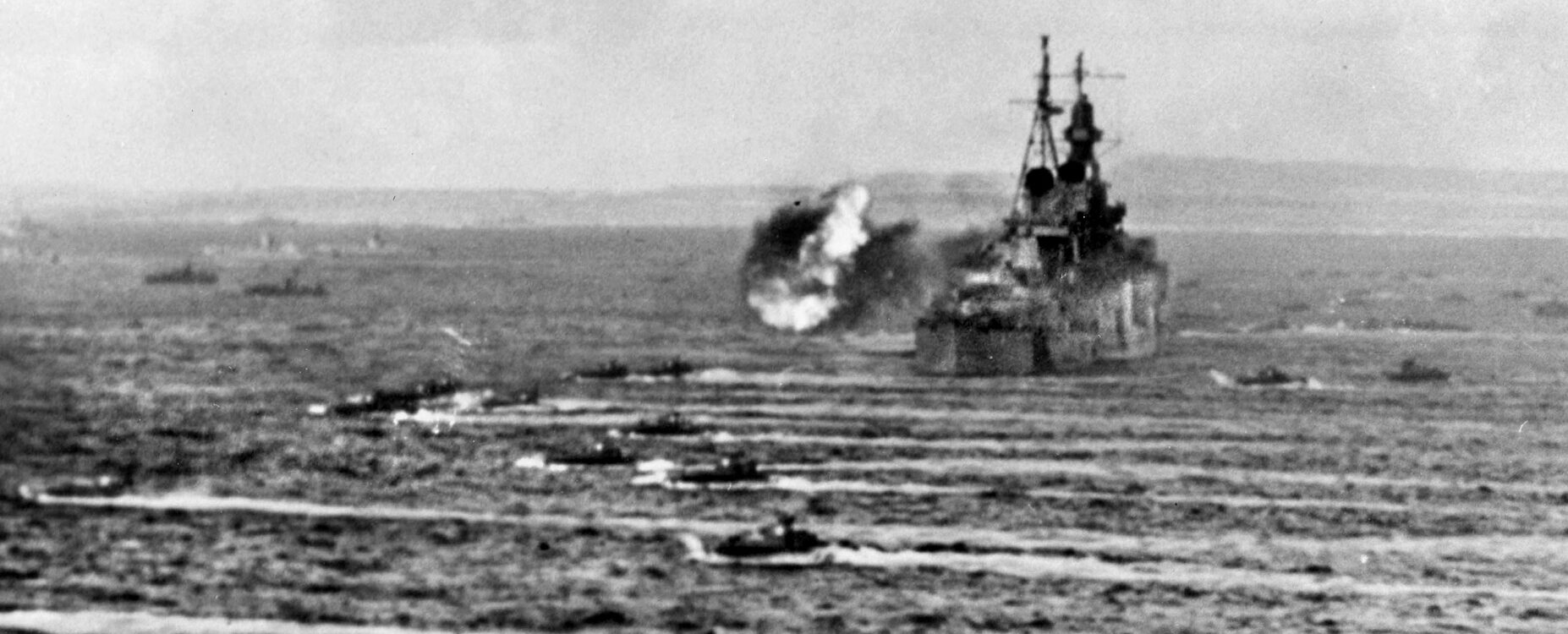 The Indy fires a broadside with her 8-inch guns at Japanese positions on Saipan as landing craft (foreground) head for the invasion beaches, July 1944.