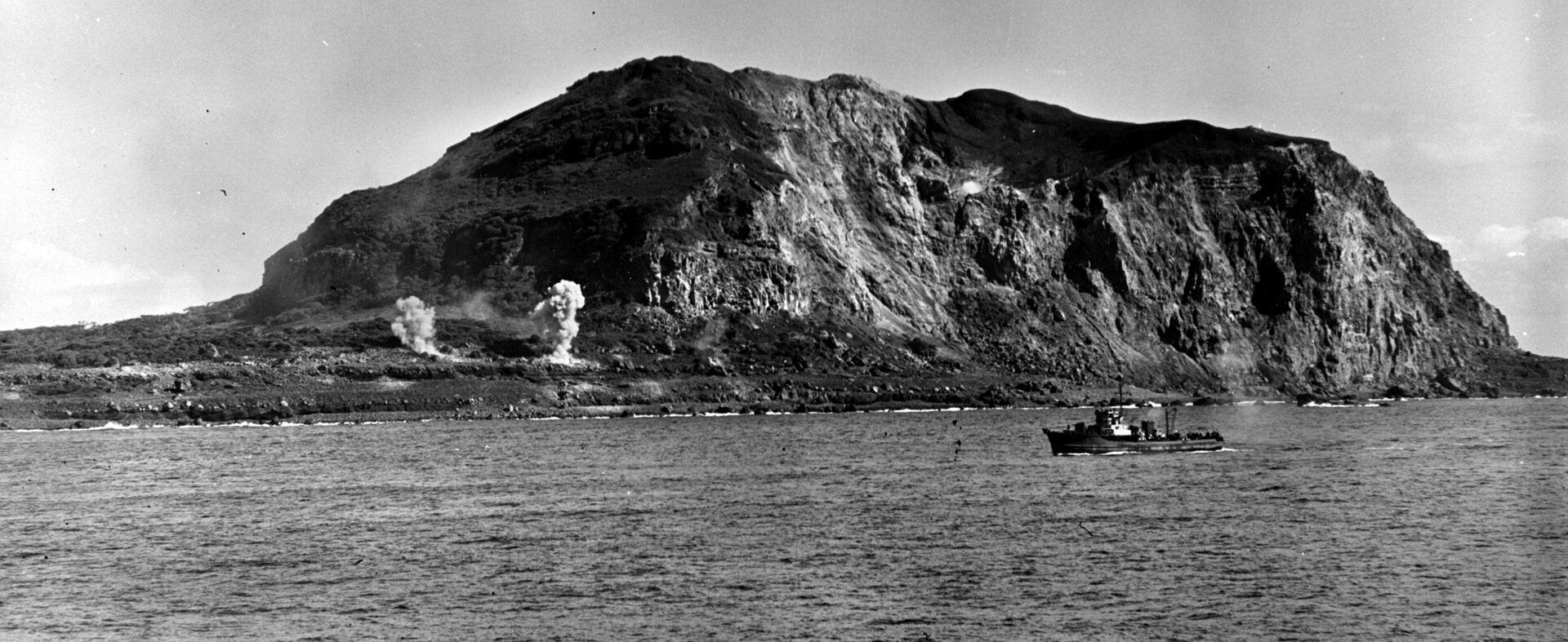 A U.S. Navy patrol boat cruises near the shore as naval gunfire explodes along the base of Iwo Jima’s Mount Suribachi on D-Day-minus-two, February 17, 1945. The Indianapolis supported the operation. 