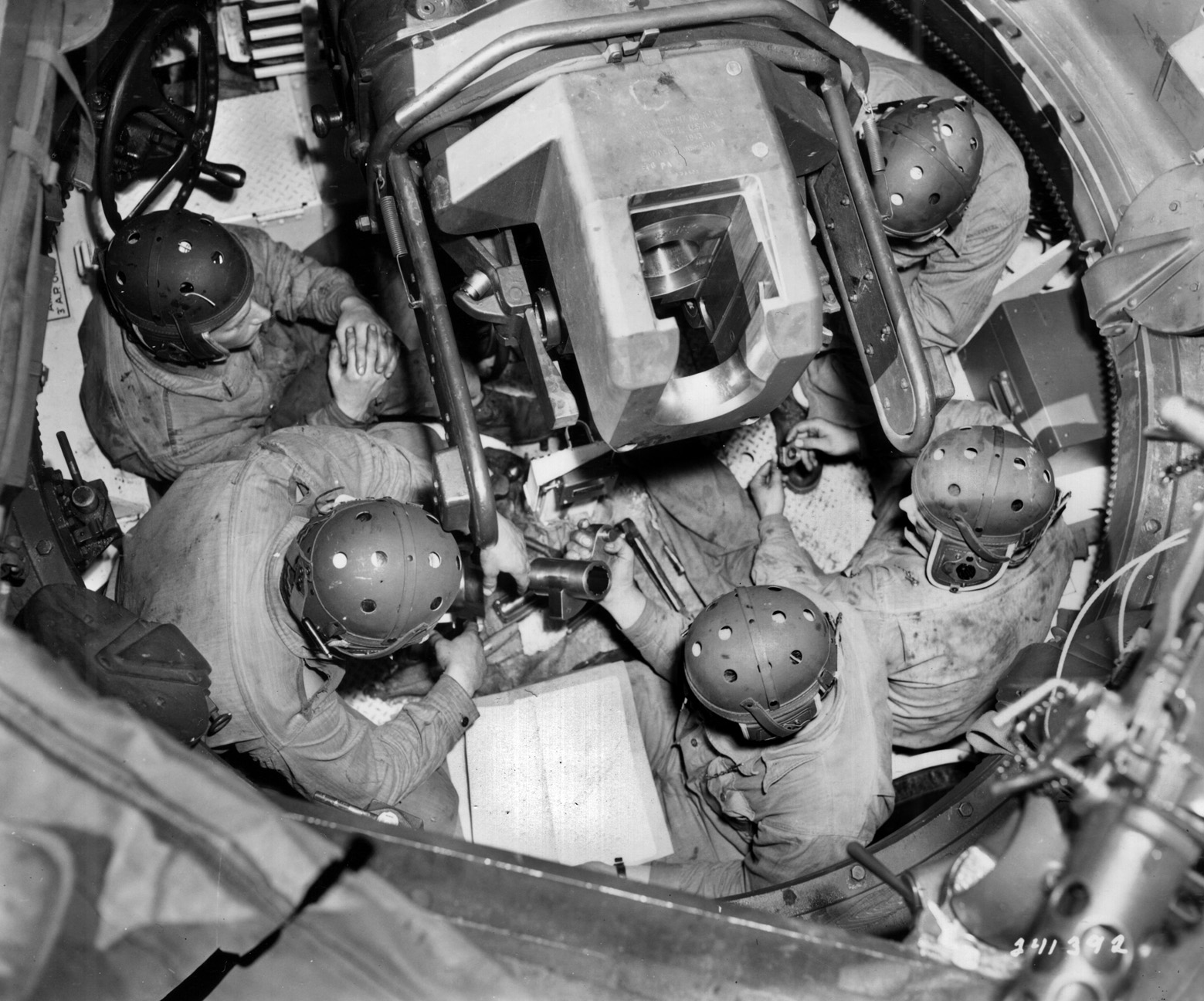 Looking down into the open turret of an M10, a crew is observed practice-loading the 3-inch gun. 