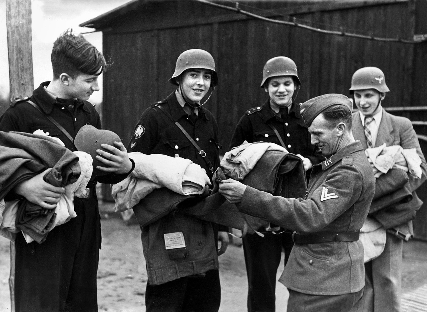Smiling Hitler Youth members, one still in civilian coat and tie, are issued their equipment from an NCO in the Luftwaffe.