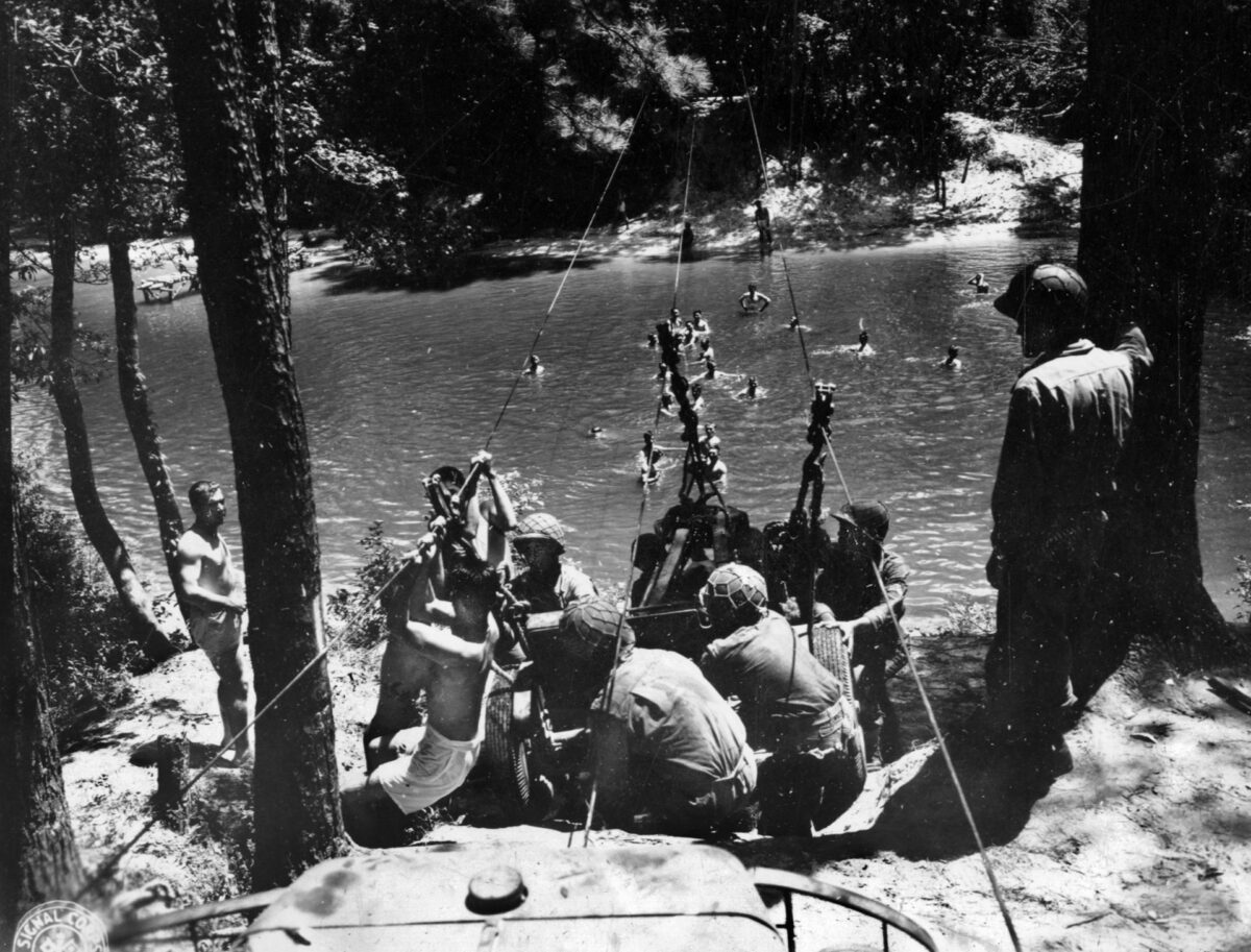 Members of a 442nd RCT anti-tank company, while training at Camp Shelby, prepare to haul their gun across a stream on a raft suspended from steel cables and pulled by the men in the water, August 19, 1943. 