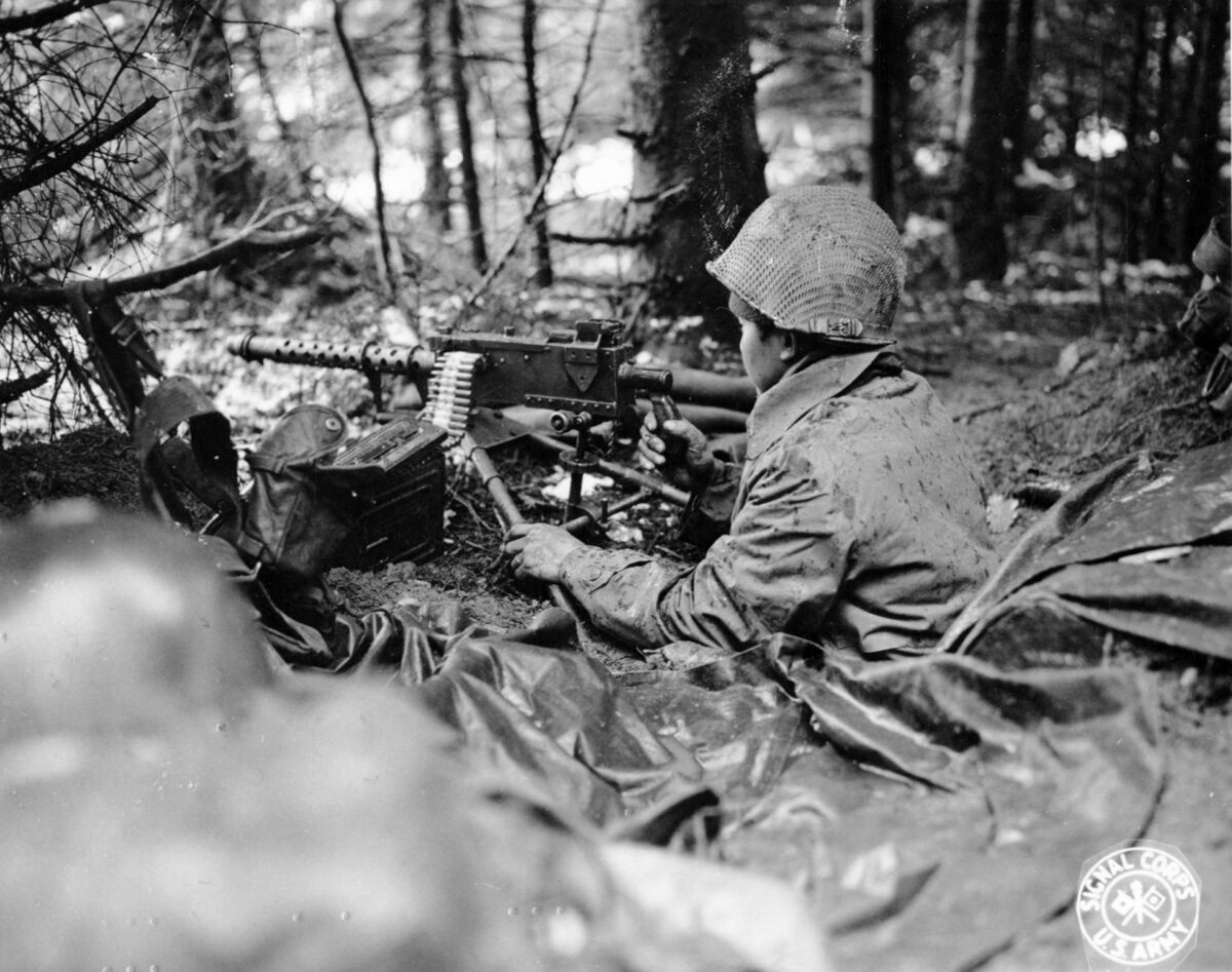 A Nisei soldier, protected from the foul weather with a raincoat, mans a .30-caliber air-cooled machine gun in the Ste. Die area of the front, November 1944. 