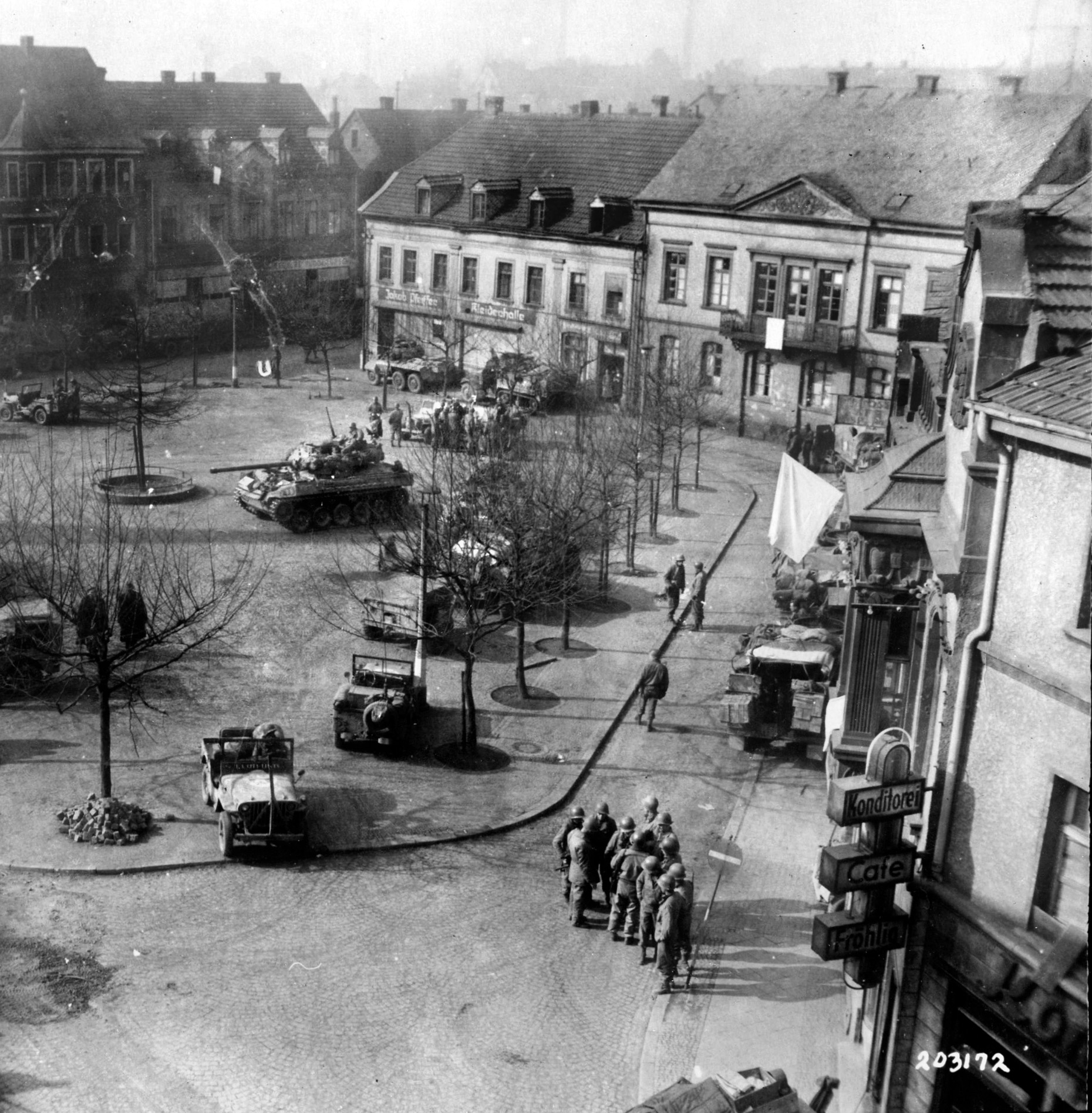 10th Armored Division troops and vehicles crowd the town square of St. Wendel, 30 miles southeast of Trier. White flags indicate the citizenry has surrendered. 