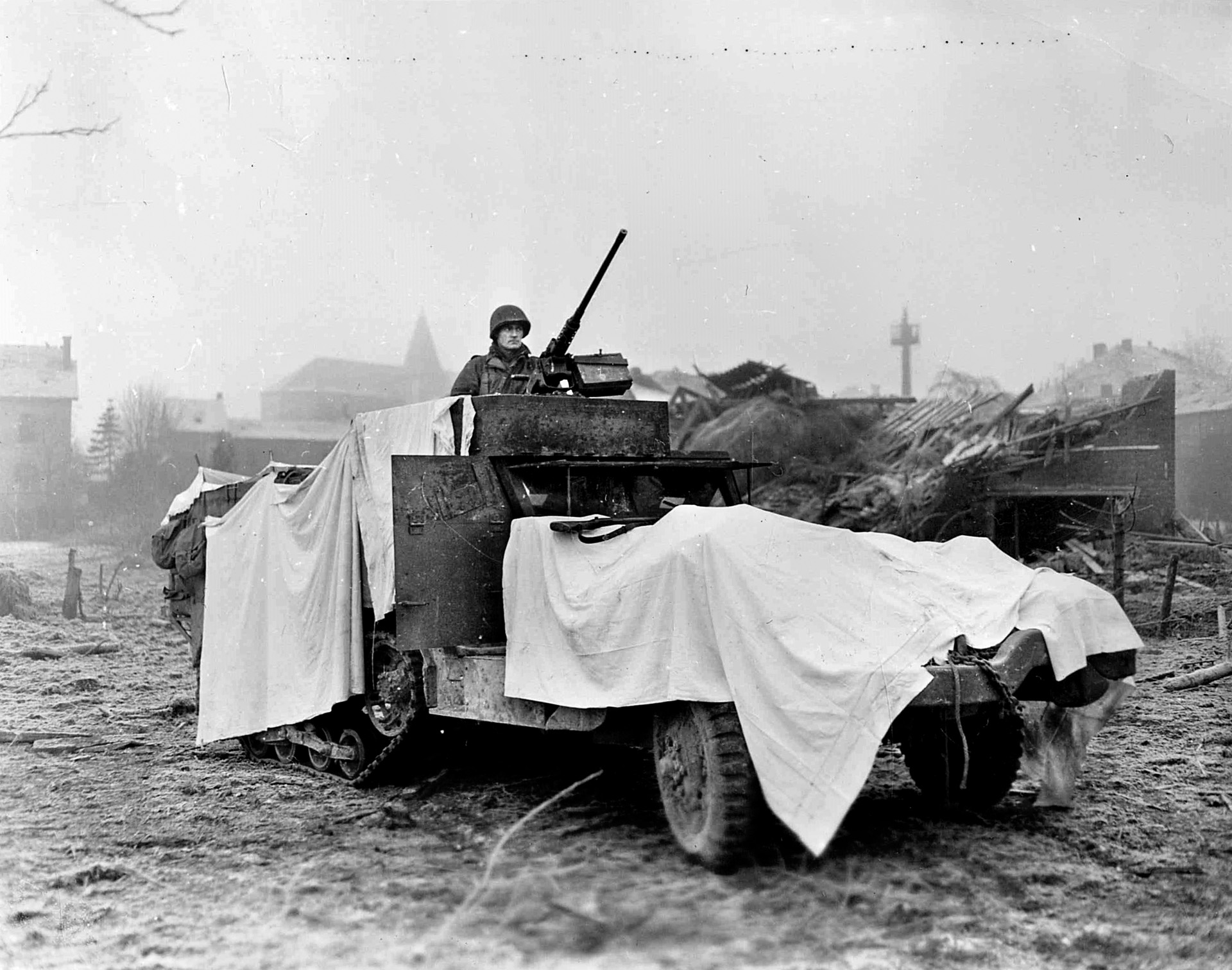 10th Armored Division crewman Walter Streetman mans his .50-caliber machine gun during the fighting around Bastogne. His vehicle is camouflaged with white sheets in an effort to blend in with the expected coming snow. 