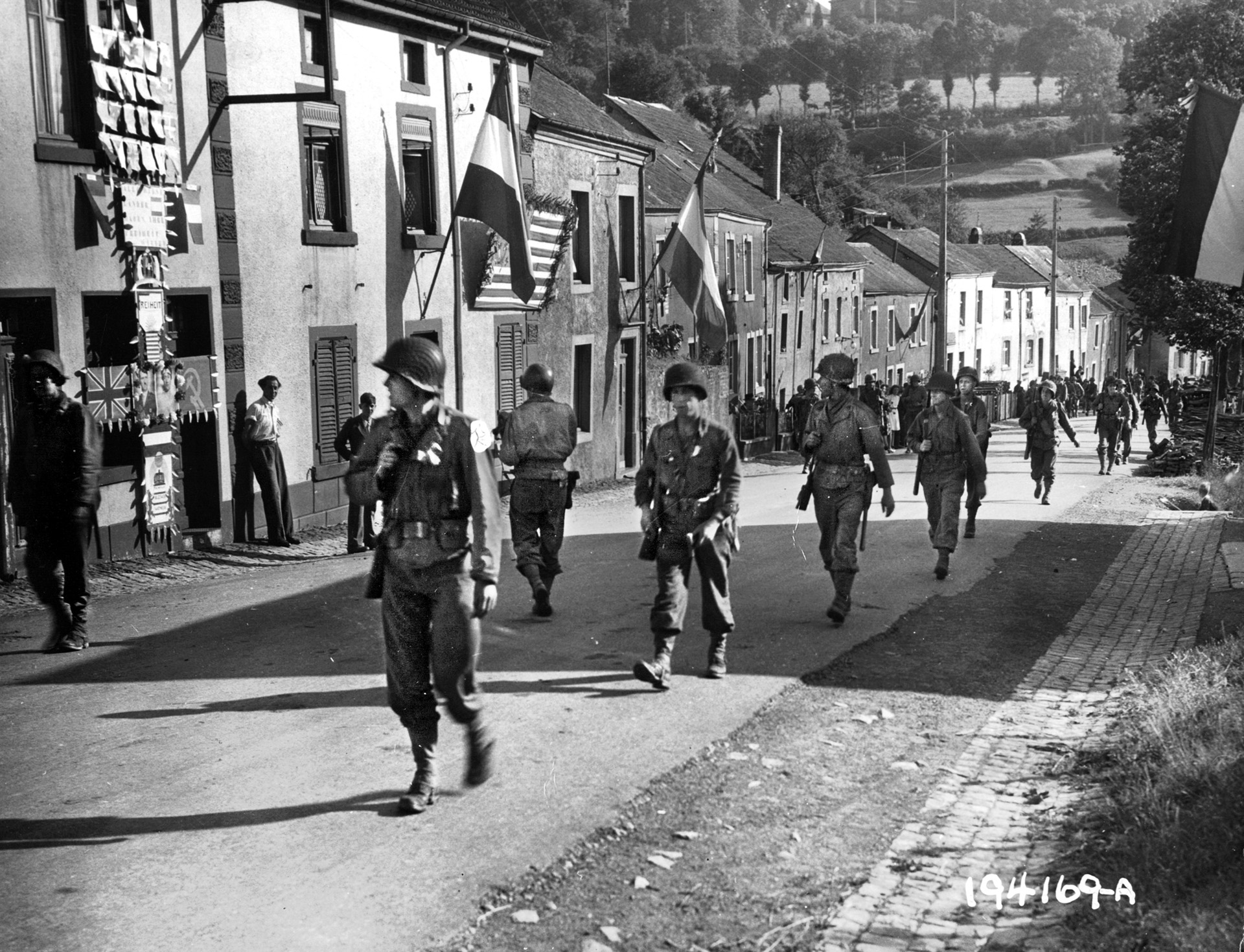 American troops of the 2nd Battalion, 109th Infantry Regiment, 28th Infantry Division, march through a flag-bedecked Luxembourg town in pursuit of the enemy on September 10, 1944. 