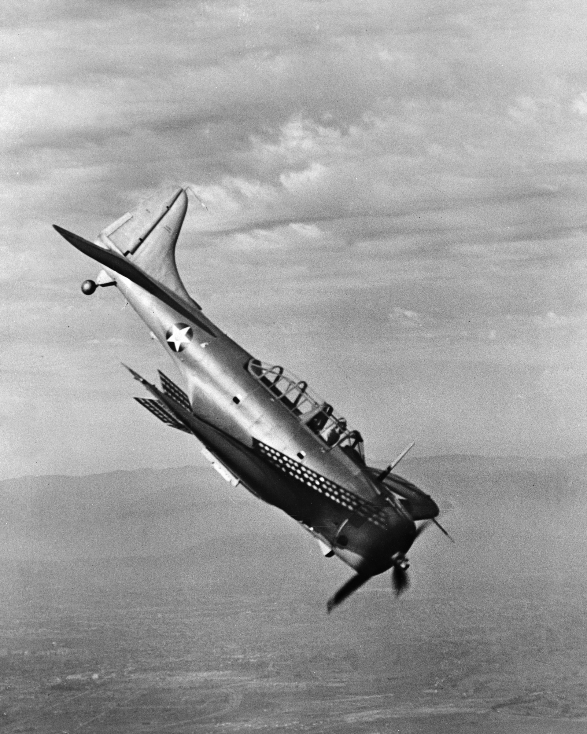 A Douglas A-24 Banshee dive bomber begins a steep dive during training exercises. The 27th Bomb Group flew worn- out Banshees during its service. Note the dive brakes.