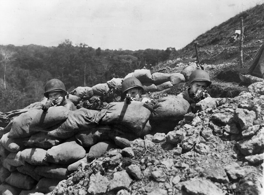 Behind their sand-bag reinforced foxhole, three U.S. Marines point their rifles in the direction of a suspected Japanese attack on Edson’s Ridge.