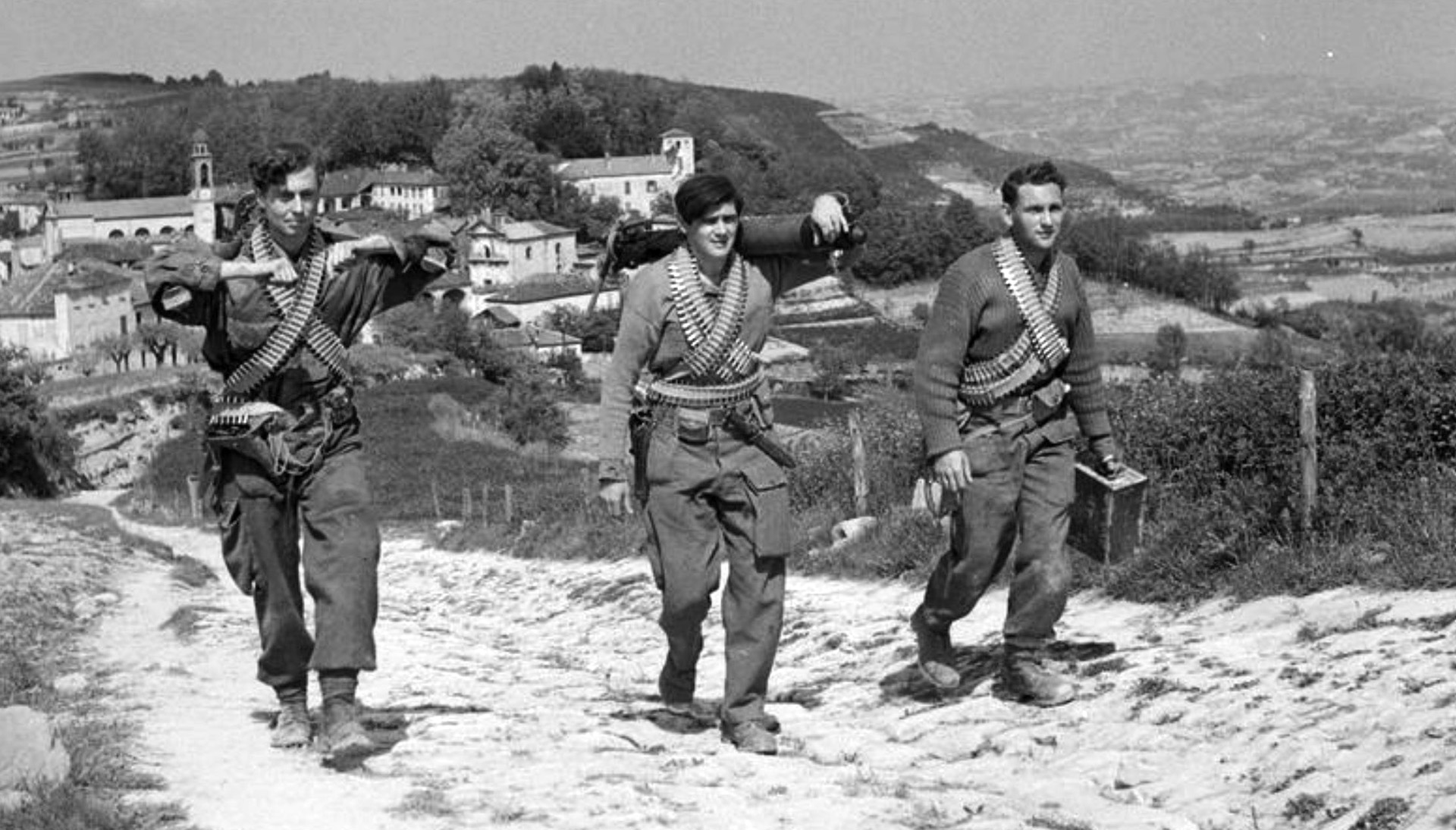During an operation to assist Italian partisans, heavily armed men of No. 2 SAS Regiment carry components of Vickers machine guns and ammunition belts draped over their shoulders as they traverse a mountain path somewhere in the countryside of Italy.
