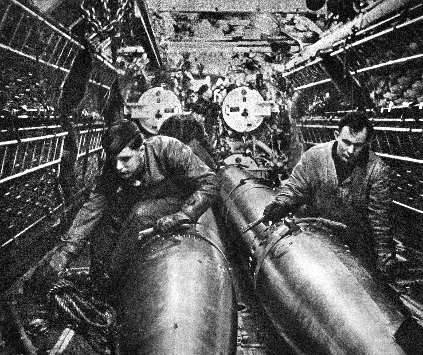 The cramped quarters aboard Nazi U-boats are visible in this image of crewmen working feverishly in the torpedo room aboard one of the German submarines. The sailors are handling torpedoes for use in the tubes, which are visible at the rear. 