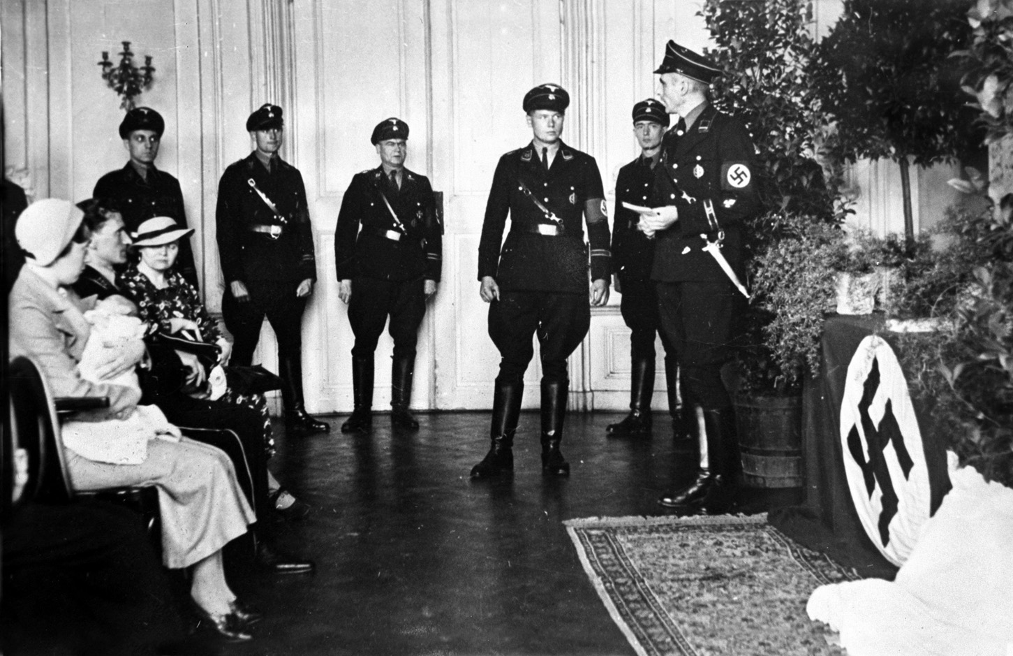 During the ‘baptism’ of a Lebensborn baby in Nazi Germany, the mother holds the infant while the father is to the right. SS soldiers look on during the ceremony, which takes place before a Swastika emblazoned altar of sorts. 