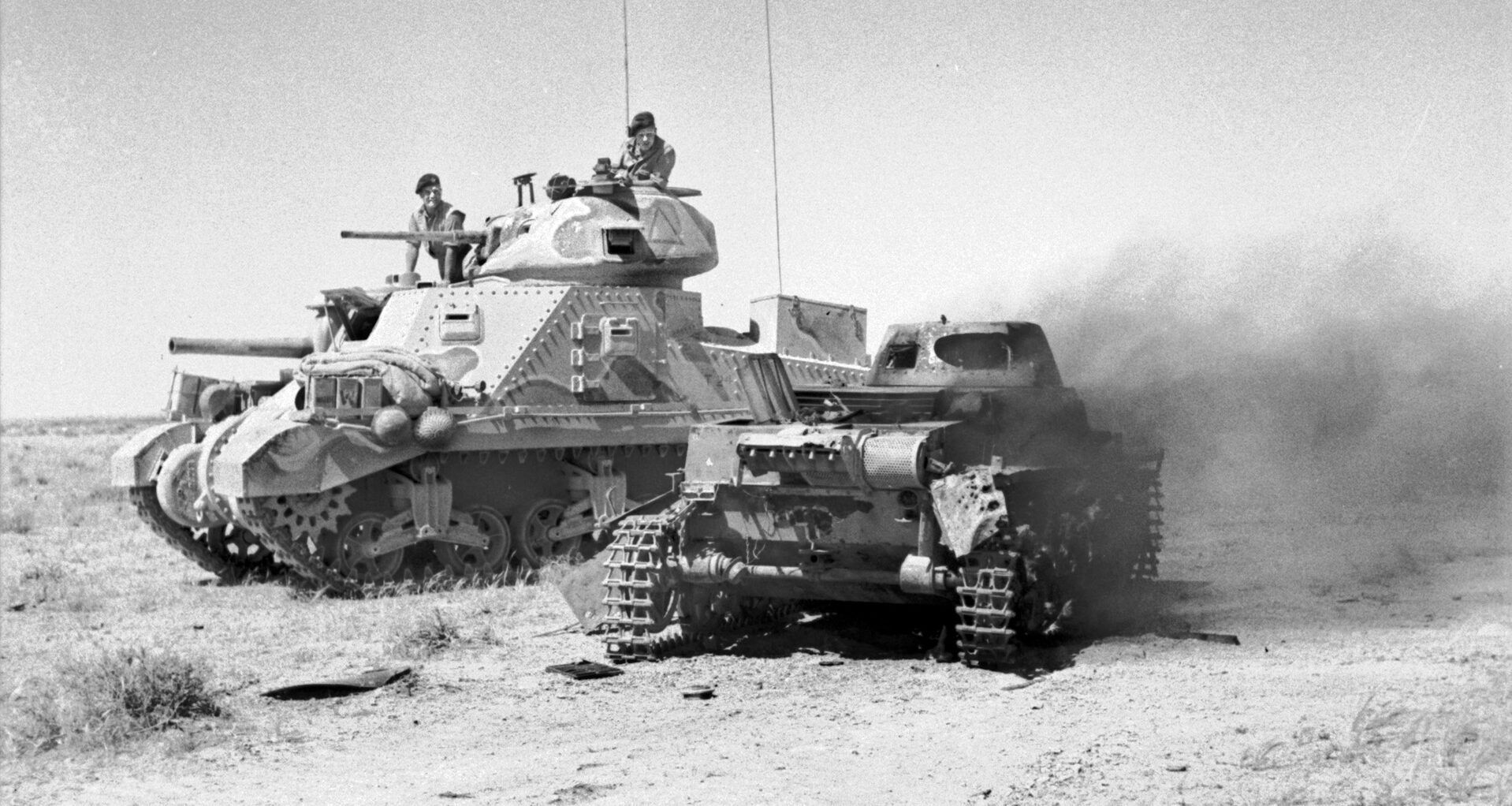 In this image, a German vehicle has come to grief. An American-built M3 Grant tank passes the blasted hulk of an Axis tank as its British crew surveys the wreckage. The Germans were reportedly surprised by the appearance of the Grant on the battlefield at Gazala.