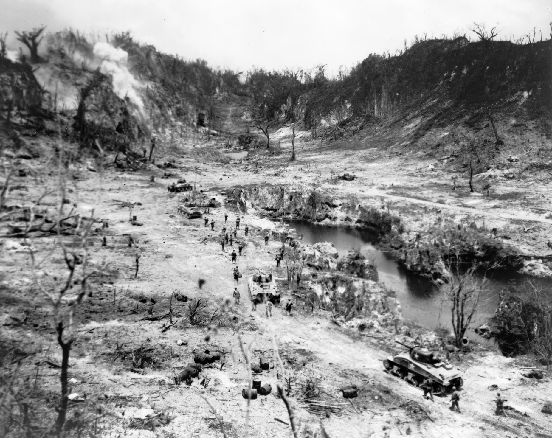 Marine artillery saturates the mouths of caves that the Japanese have fortified, while riflemen attack the positions, often resorting to explosive satchel charges to silence the enemy emplacements and then calling on bulldozers to seal the entrances, entombing the occupants.