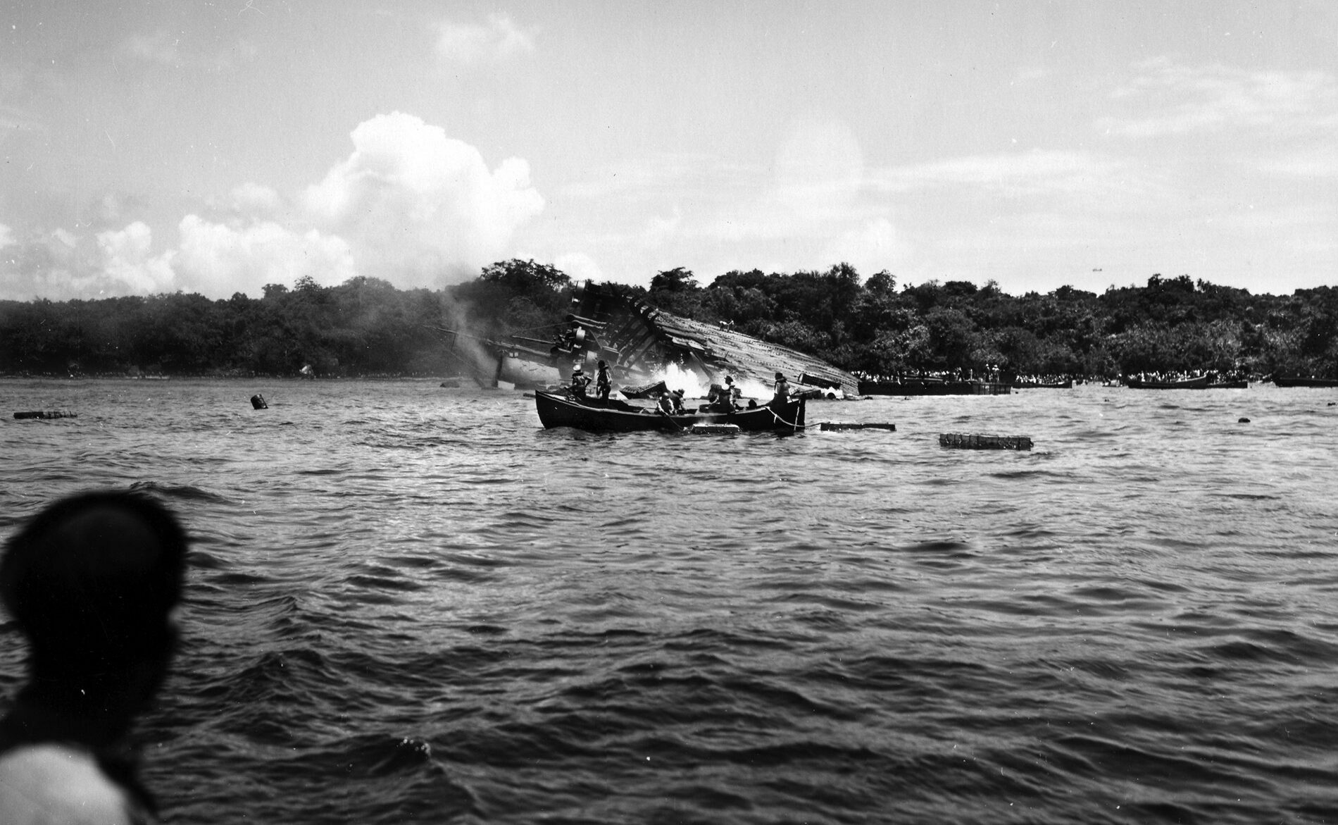 This photo was taken just moments before the Coolidge slid beneath the surface of the harbor at Espiritu Santo. In the distance, two men are visible atop the hull of the stricken vessel. These may well be Captain Warren K. Covill and Warrant Officer Robert H. Moshimer, who were assisting Captain Elwood Euart, who lost his life while searching for anyone trapped inside the sinking ship.