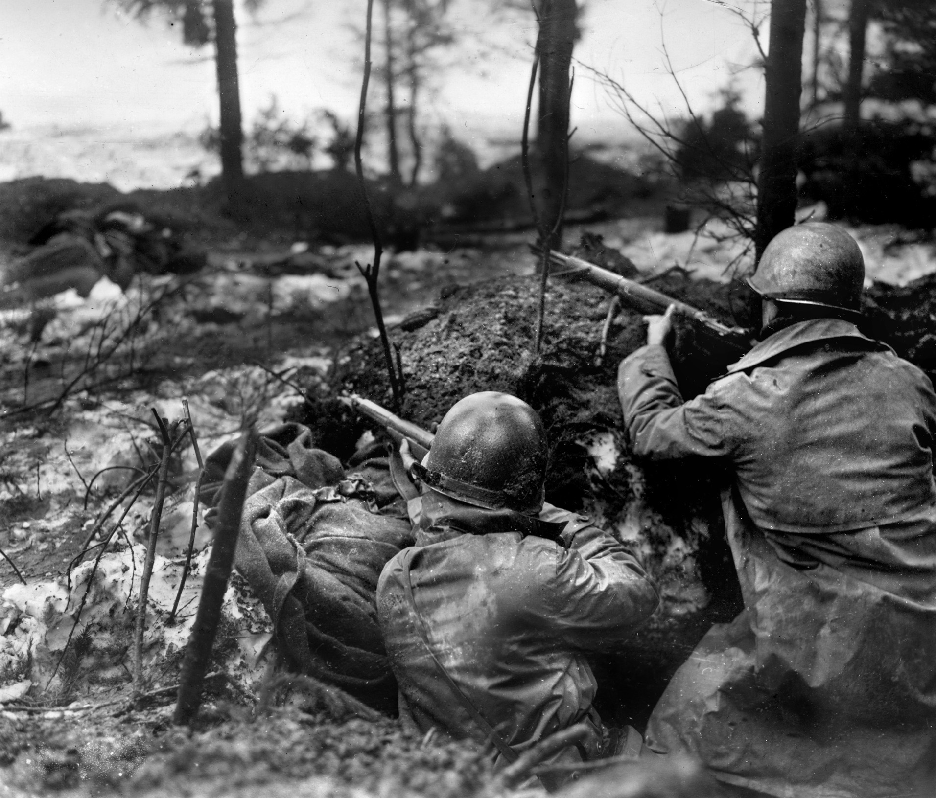 Their foxhole reinforced with logs, a pair of American soldiers of the 99th Infantry Division watch and wait for a German attack during the Battle of the Bulge. The heroic stand at Lanzerath by 20 year old Lt. Bouch and the 21 men under his command slowed the advance of Kampfgruppe Peiper.