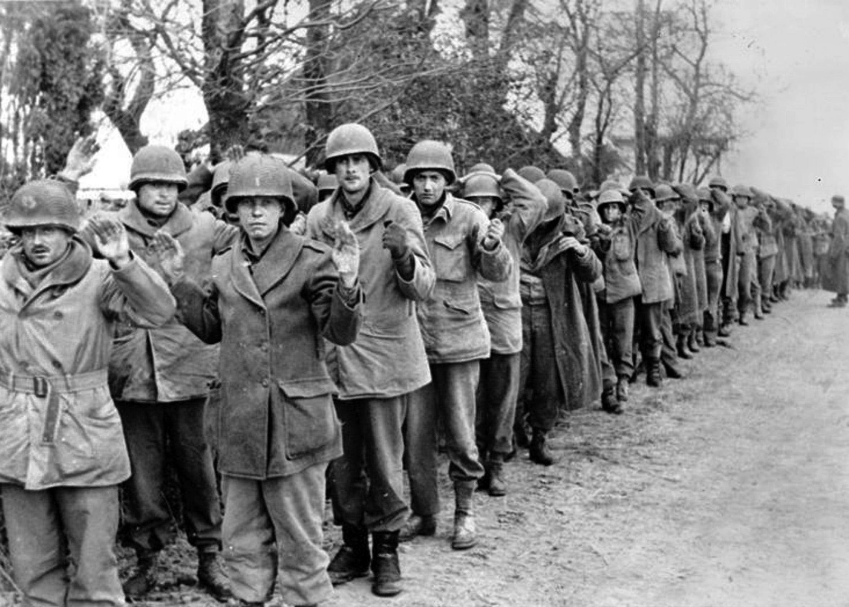 Dazed and confused, American soldiers captured by the Germans during the opening phase of the Battle of the Bulge march with their hands in the air toward an uncertain fate. The stand by the 394th I&R Platoon at Lanzerath was critical in slowing the German advance.