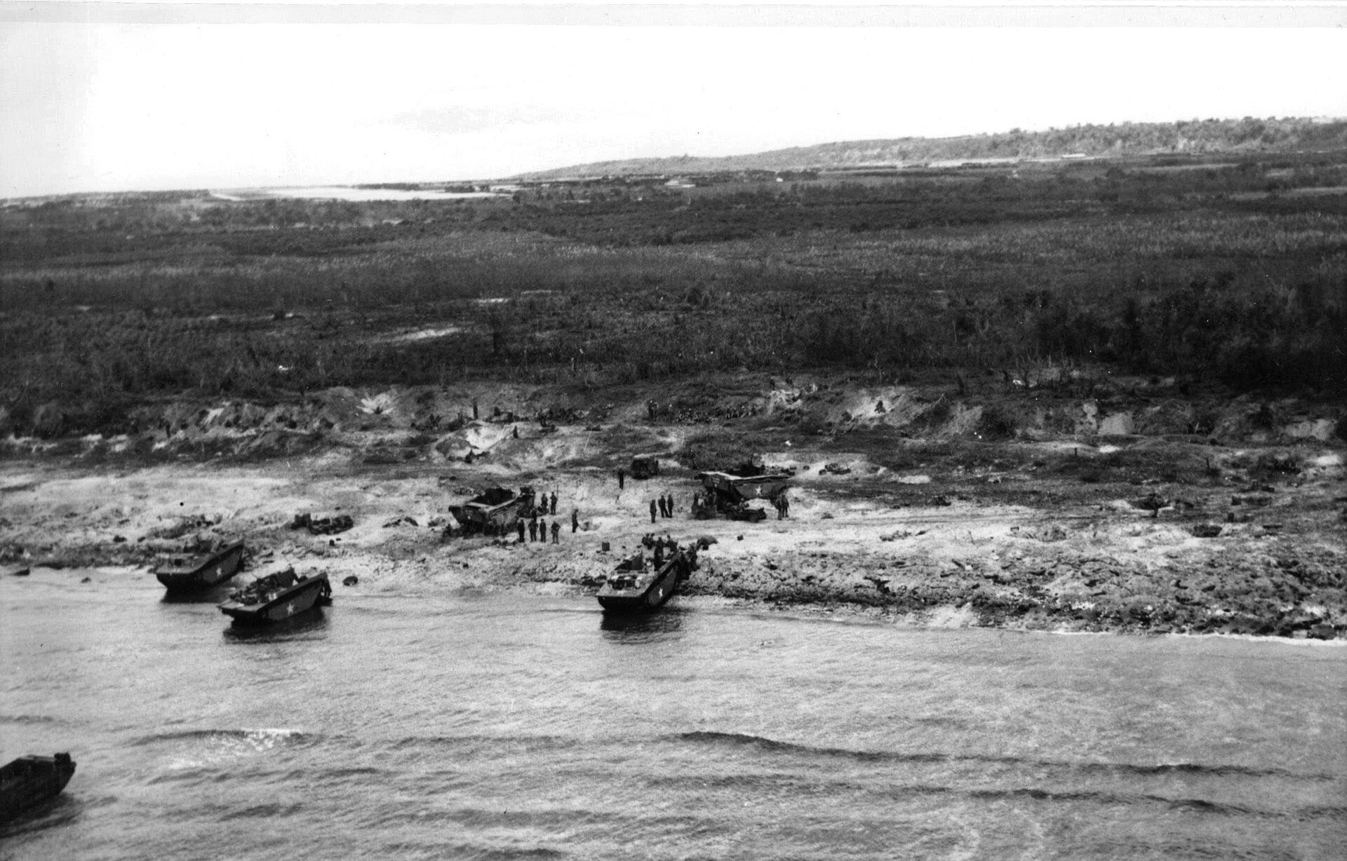 Marine foxholes dot the area near a landing beach on the island of Tinian as amphibious landing craft continue to bring troops and supplies ashore. Tinian later became a substantial air base for American heavy bombers.