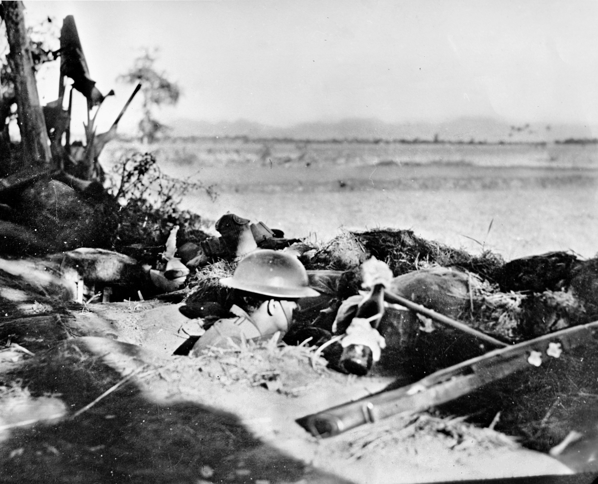 From his defensive position on the Bataan Peninsula, an American soldier watches the horizon for signs of the Japanese invaders. The soldier is armed with his government-issue rifle and a Molotov cocktail, simply a bottle filled with gasoline to be lit and thrown at enemy vehicles.