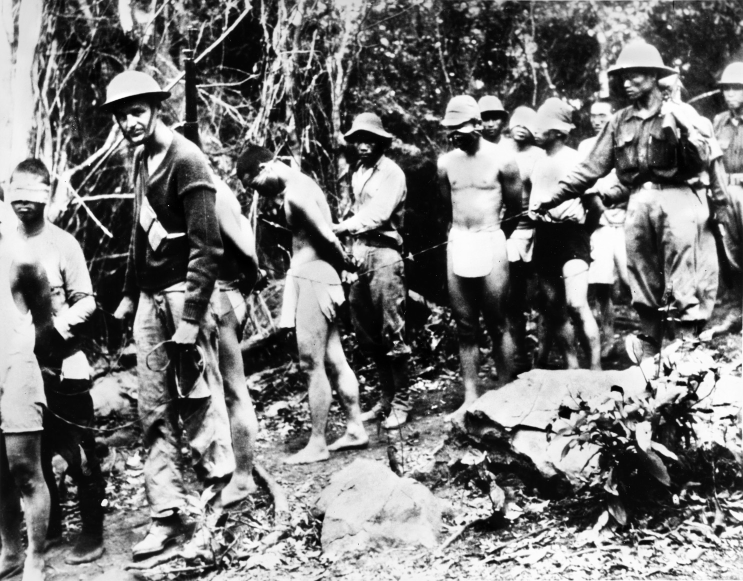 Blindfolded with their hands bound behind their backs, Japanese soldiers captured while trying to infiltrate American lines by swimming along the western shore of the Bataan Peninsula are led by their captors to American headquarters for questioning.