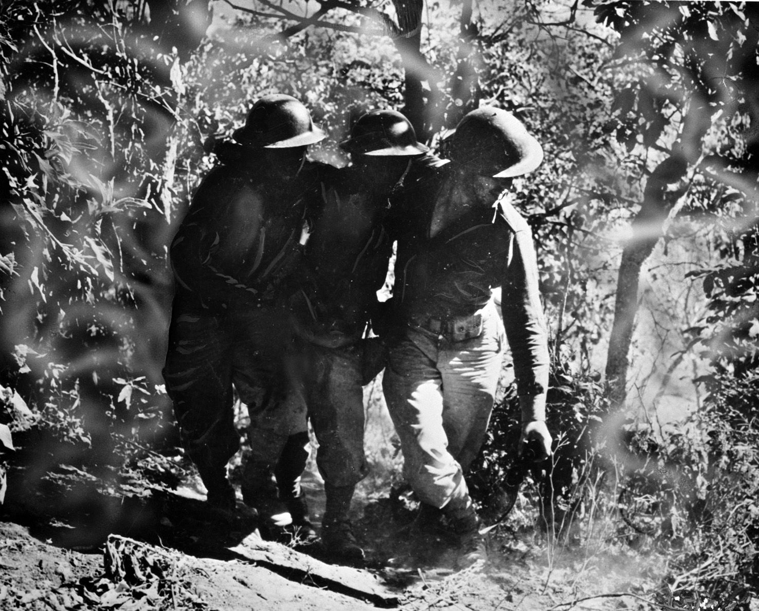 A soldier wounded during fighting along the west coast of Luzon is helped to an aid station at Longoskawayan Point by a pair of comrades. This image was taken in January 1942.