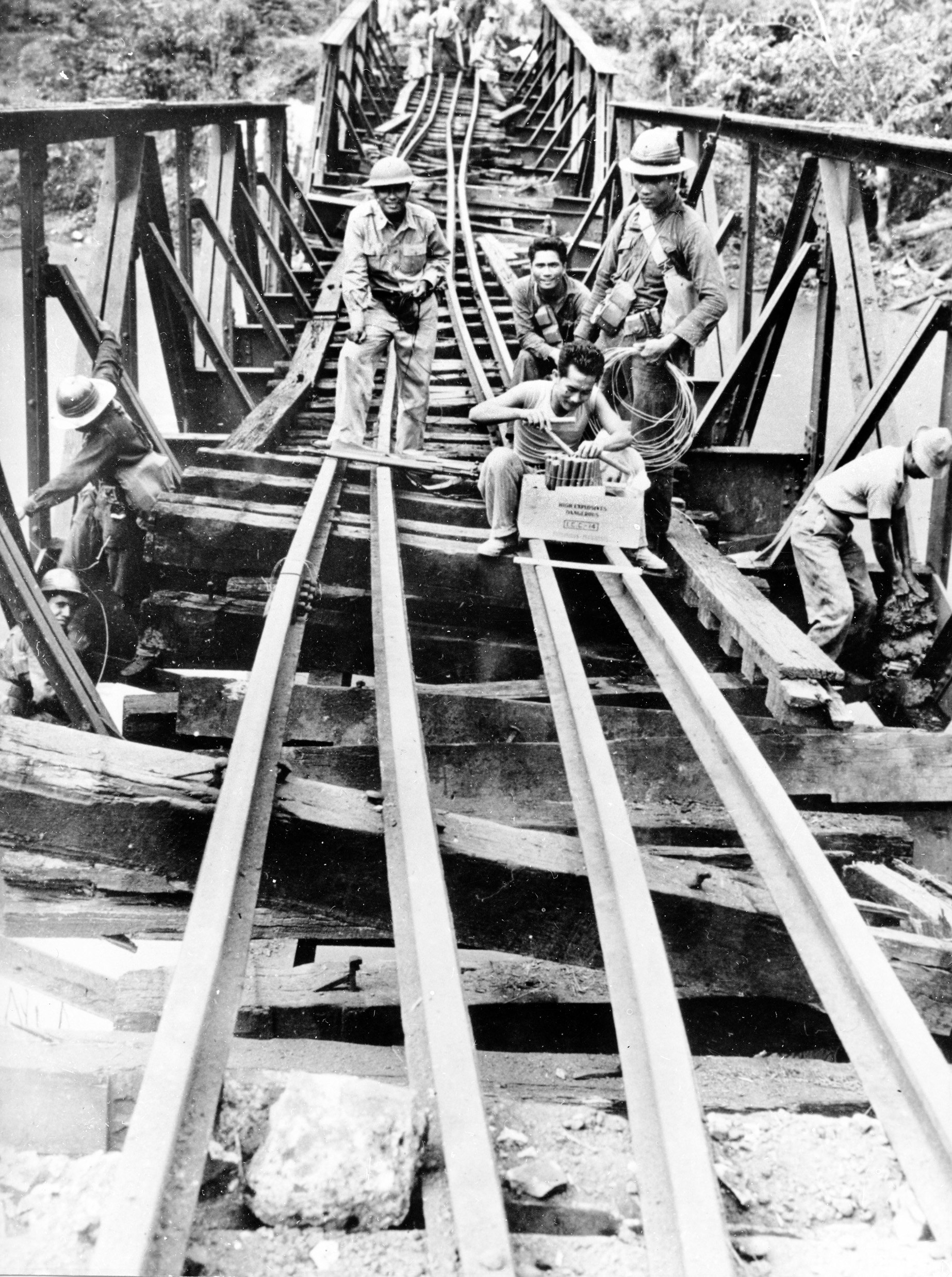 Preparing explosive charges, Filipino engineers rig a bridge on the island of Luzon for demolition after General Douglas MacArthur ordered such measures to impede the progress of the invading Japanese in the Philippines. Such measure sought time for the defenders to retire to Bataan and Corregidor.