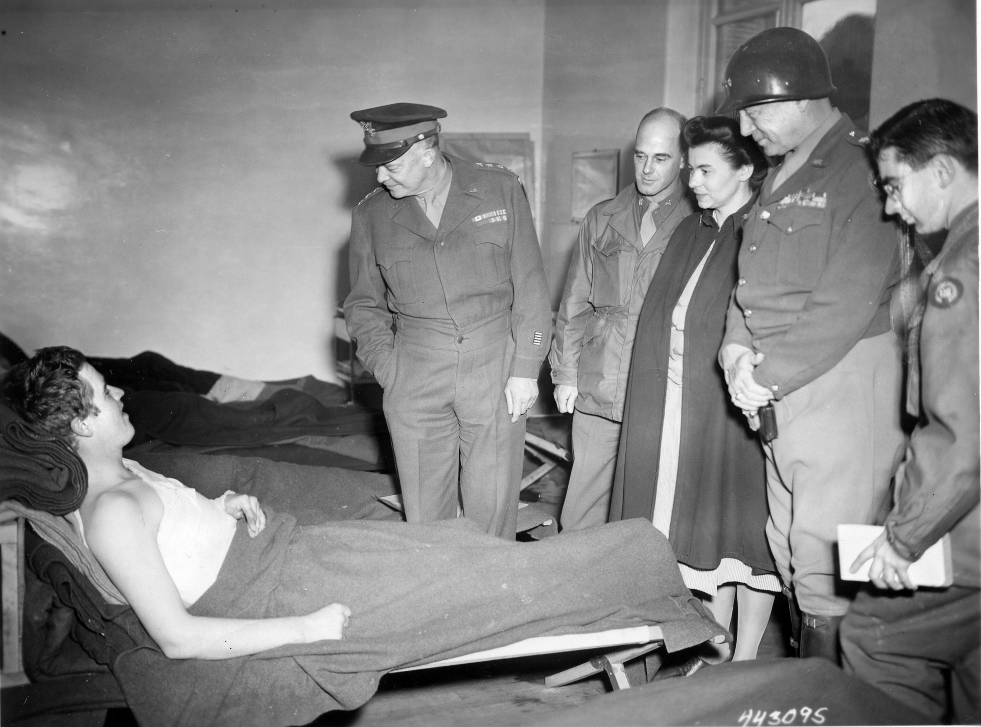 Eisenhower and Patton talk to Private Paul D. McDaniel of Maumee, Ohio, at the 12th Evacuation Hospital, while a doctor, nurse, and reporter look on. 