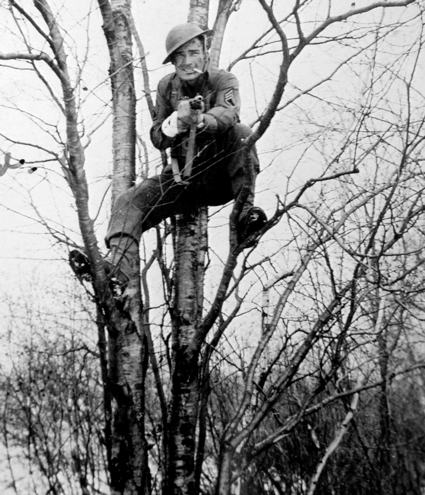 During a lighter moment of training, Alven Baker, wearing the rank of a staff sergeant and smoking a cigarette, has climbed a tree to pose for a photographer. 