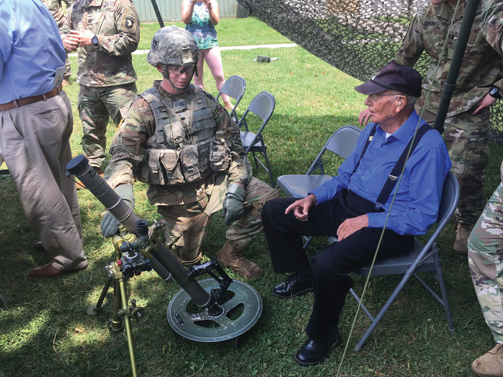 Farmer and Easy Company veteran Brad Freeman listens as a soldier from today’s Easy Company explains the features of a modern mortar. Freeman was impressed with the condition of America’s soldiers today.