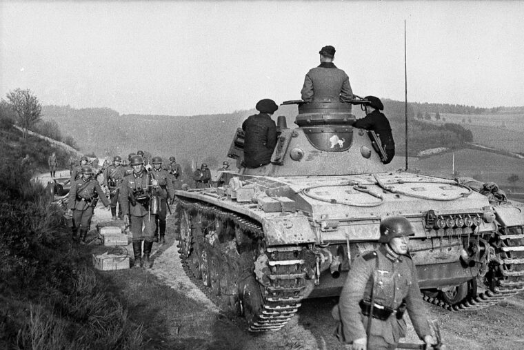 German infantrymen march past a PzKpfw. III tank that has momentarily halted during the rapid advance of the Wehrmacht through France and the Low Countries in the spring of 1940. The German onslaught on May 10 shattered the uneasy months of peace that had been labeled the ‘Phony War.’