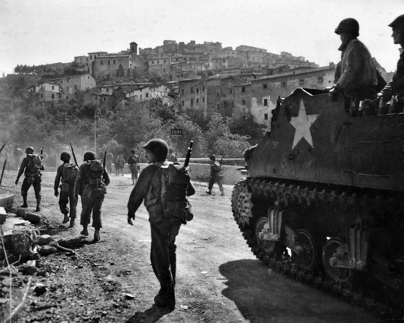 A self-propelled M7 “Priest” assault weapon mounting a 105mm howitzer pauses along a road near the town of Cori, south of Rome, as American soldiers stream past toward the Eternal City.