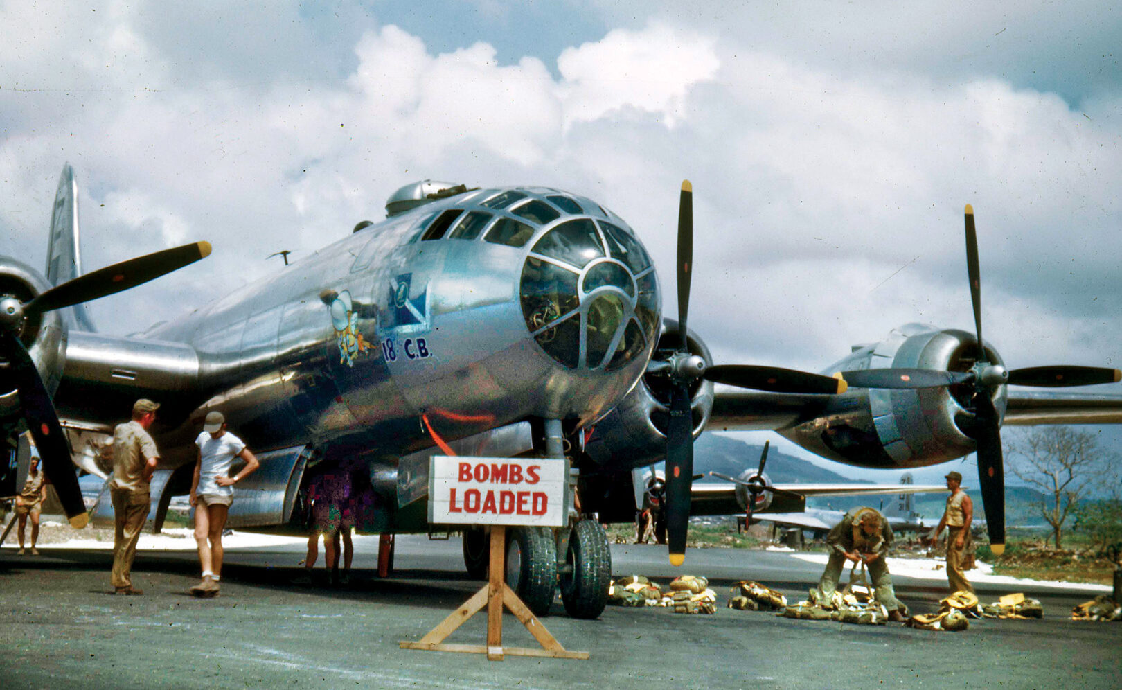 Ground crews at a base on Saipan prepare B-29 “18th C.B.” for a mission. The SeaBee mascot holding a machine gun is painted on the nose. 