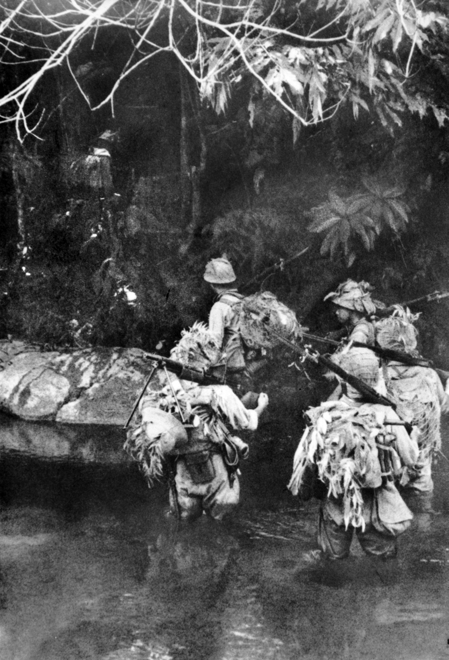 Japanese soldiers, their helmets festooned with camouflage, cross a stream during their offensive. The inhospitable terrain of the Malay Peninsula did little to slow the advance of the invading Japanese, who were well trained and disciplined.