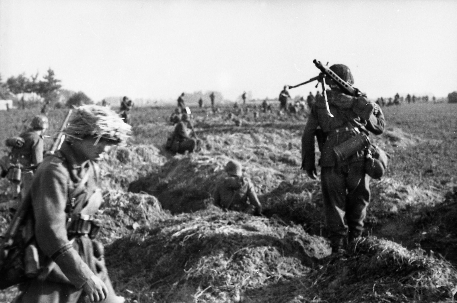 Fighting under the command of Field Marshal Erich von Manstein, panzergrenadiers of the Grossdeutschland Division of Army Group South emerge from trenches and strike out across the Russian steppe during Operation Citadel. One of the soldiers carries a light machine gun over his shoulder. 