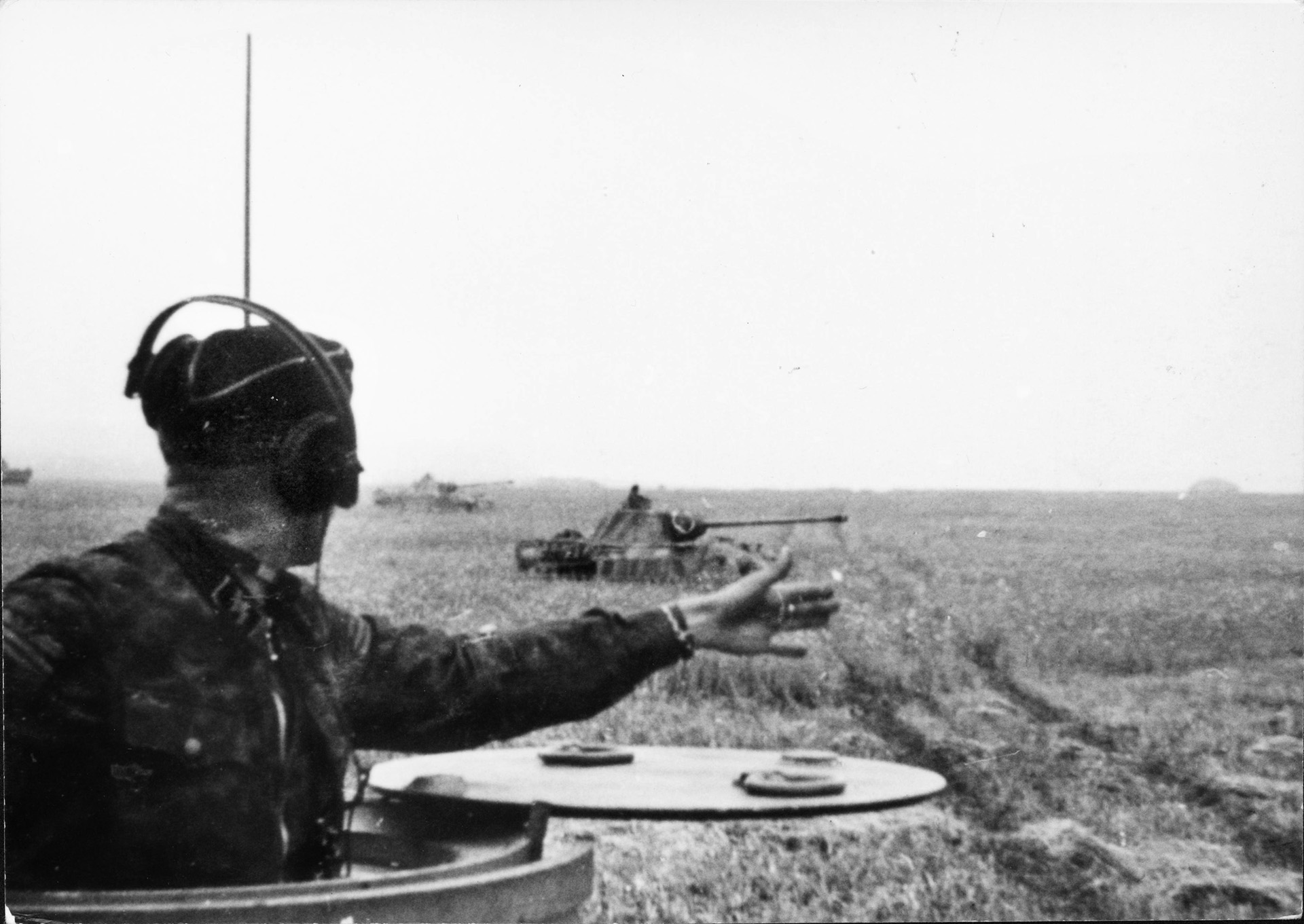 A German SS tank commander signals to another tank on his left during the advance toward the showdown with Soviet tanks at Kursk. The tank in the distance appears to be a PzKpfw. V Panther, which first appeared in significant numbers at Kursk and experienced mechanical problems.