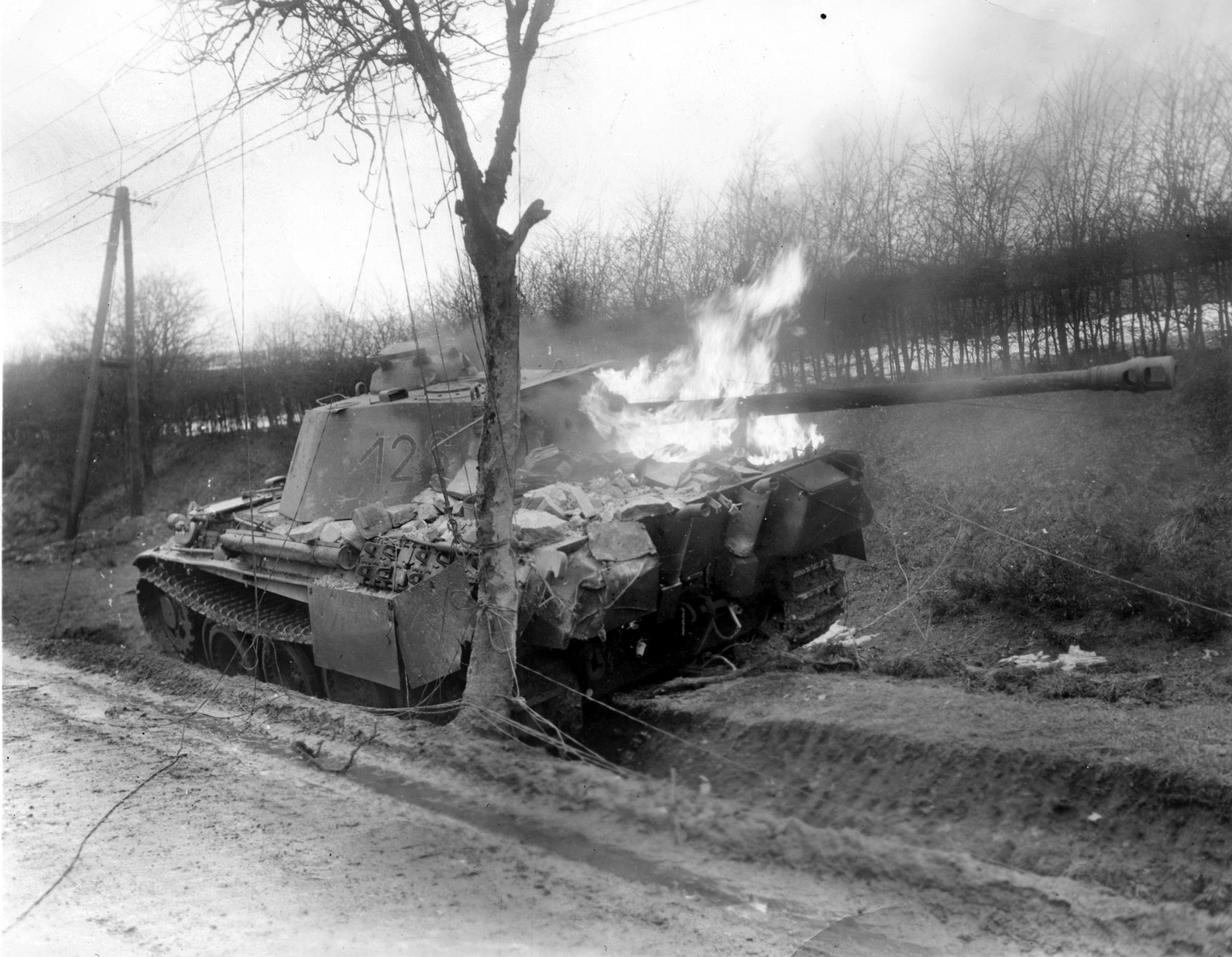 A German PzKpfw. V Panther medium tank, its long-barreled 75mm main gun jutting from the turret, blazes after being knocked out in combat in the vicinity of Bastogne, the vital Belgian crossroads town that played a pivotal role in the Battle of the Bulge. 