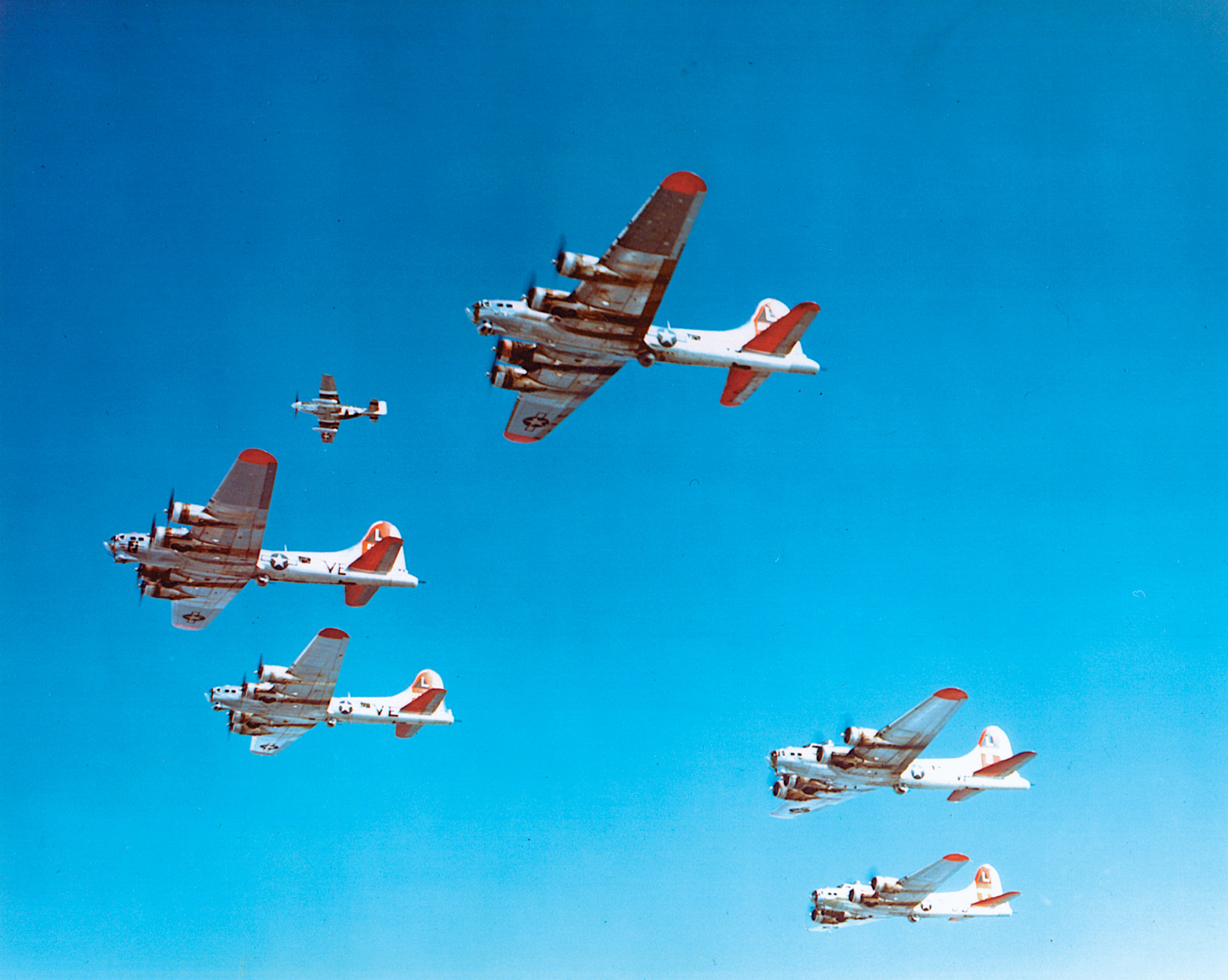 A P-51 Mustang fighter, upper left, flies escort duty with a formation of B-17 Flying Fortress bombers. The marriage of the North American airframe design and the Rolls-Royce Merlin engine produced a high-performance fighter that was originally conceived as a dive bomber powered by an Allison engine.