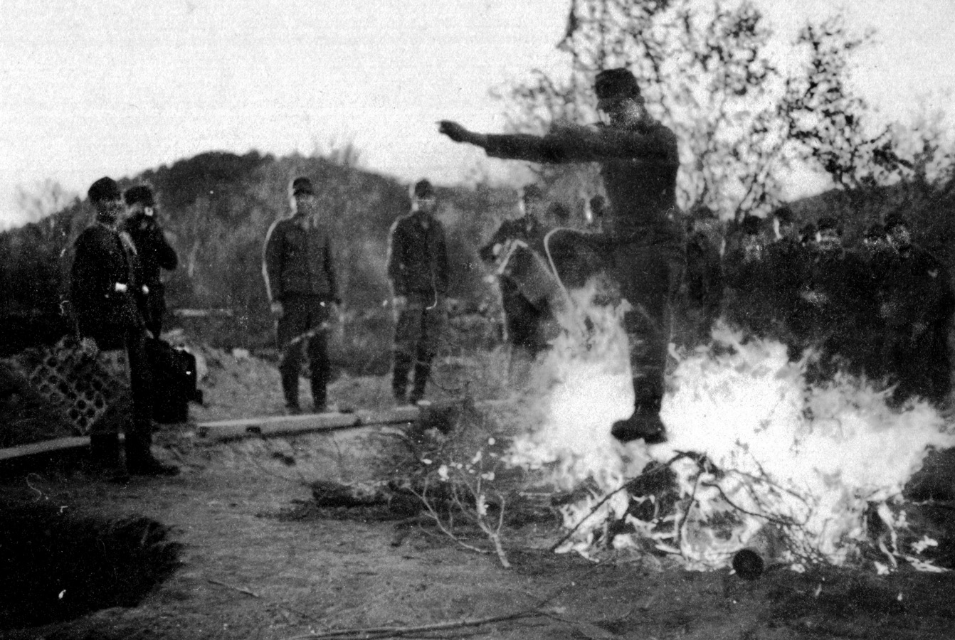 Much to the amusement of his comrades, a soldier leaps over a bonfire while another soldier (second from left) snaps his photo. Another soldier in the background appears to be holding an accordion.