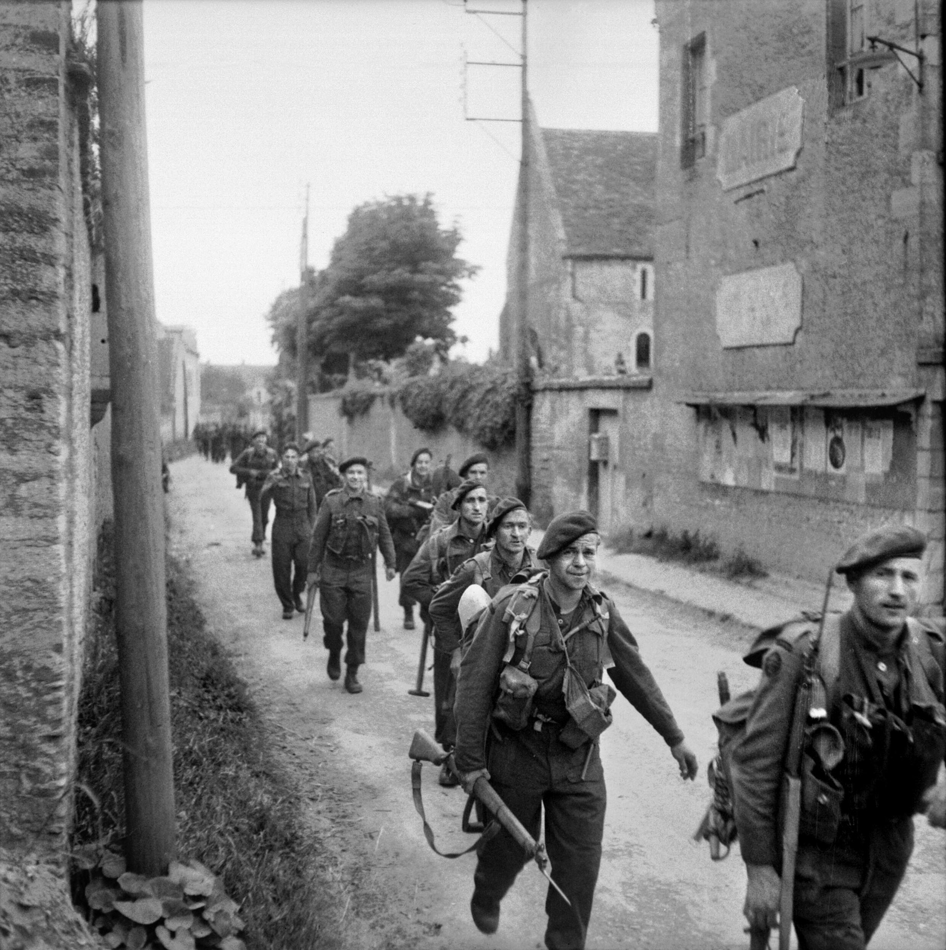 Eschewing steel helmets for berets, a group of British Commandos who have just landed at Juno Beach on D-Day, June 6, 1944, heads past the city hall (“Mairie”) of a deserted French town. Correspondent John Steinbeck considered the Commandos “very strange men.”