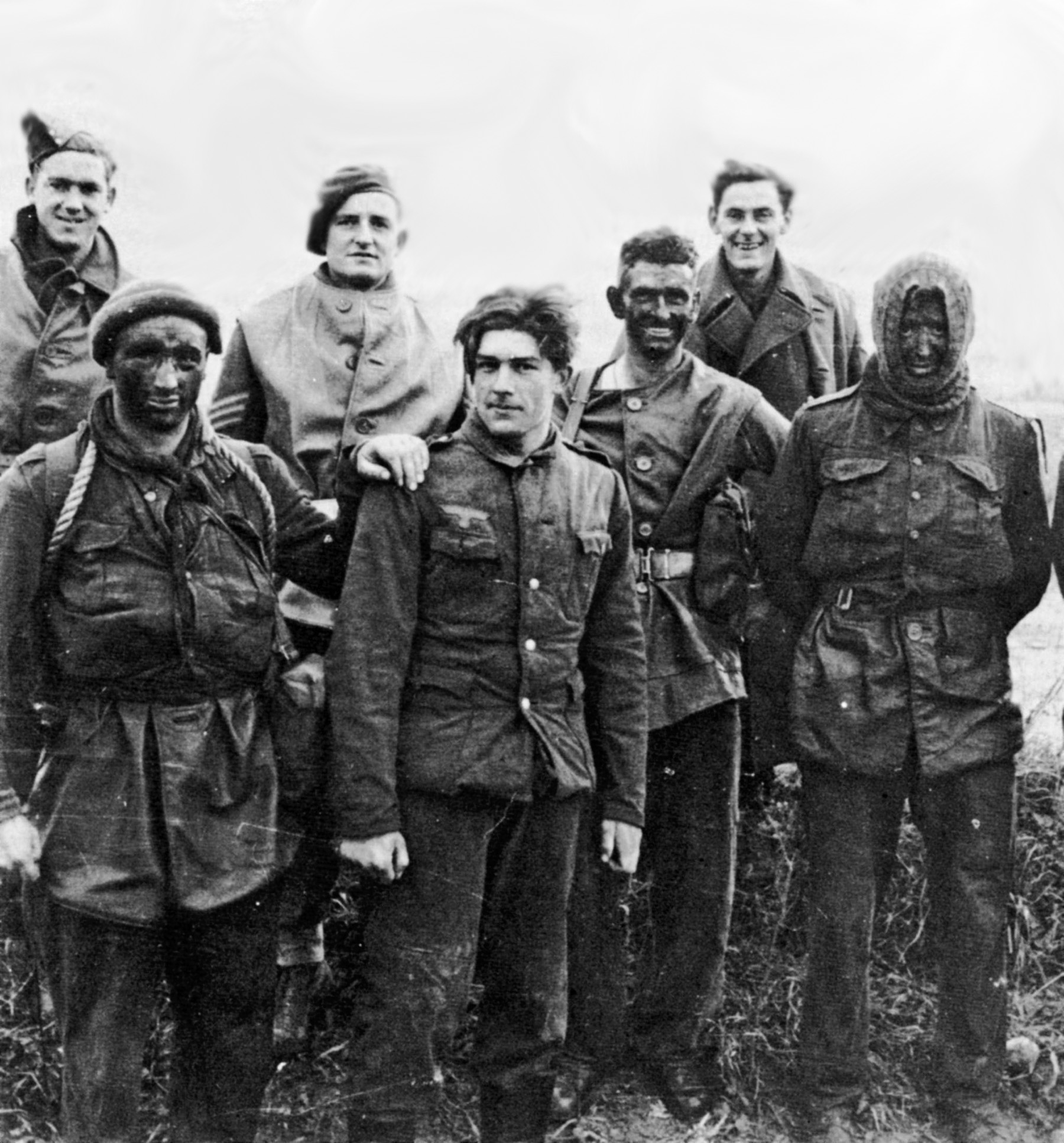 Royal Marine Commandos, some with blackened faces, pose with a captured German soldier who appears glad to be out of the fighting in Italy.