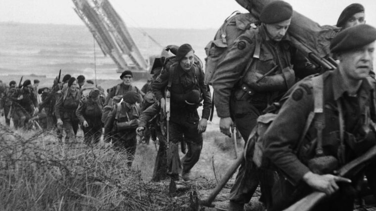 Follow-on troops of the Royal Marine Commandos, lugging their equipment, come ashore at Juno Beach, Normandy.