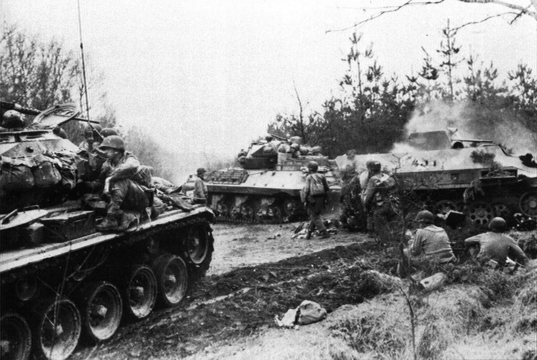 American troops and armored vehicles pause in their advance as a German Hanomag Sk.Kfz/251 (right) burns.