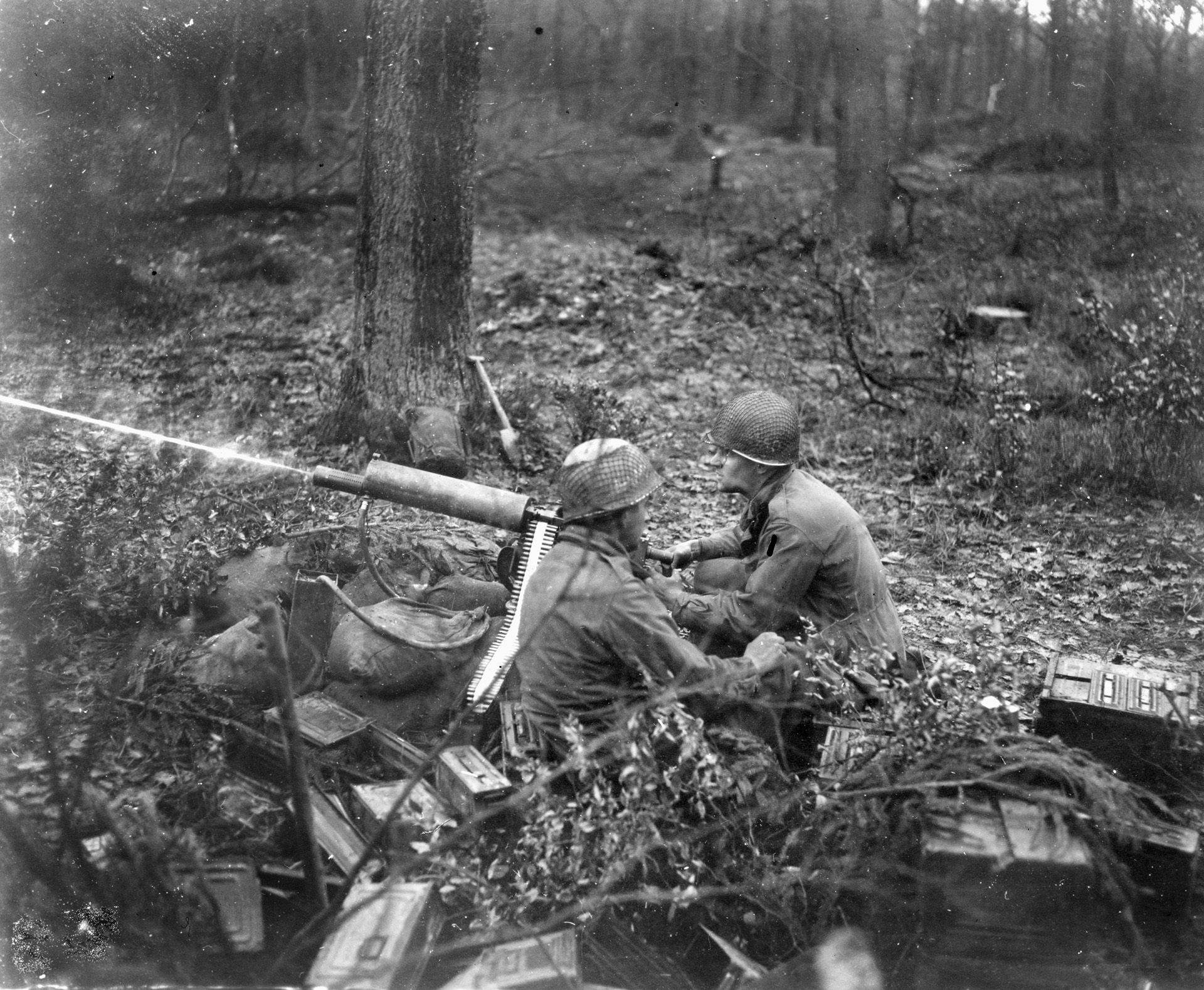 A .30-caliber machine-gun crew of Company D, 39th Regiment, 9th Infantry Division, fires a stream of bullets into the forest.