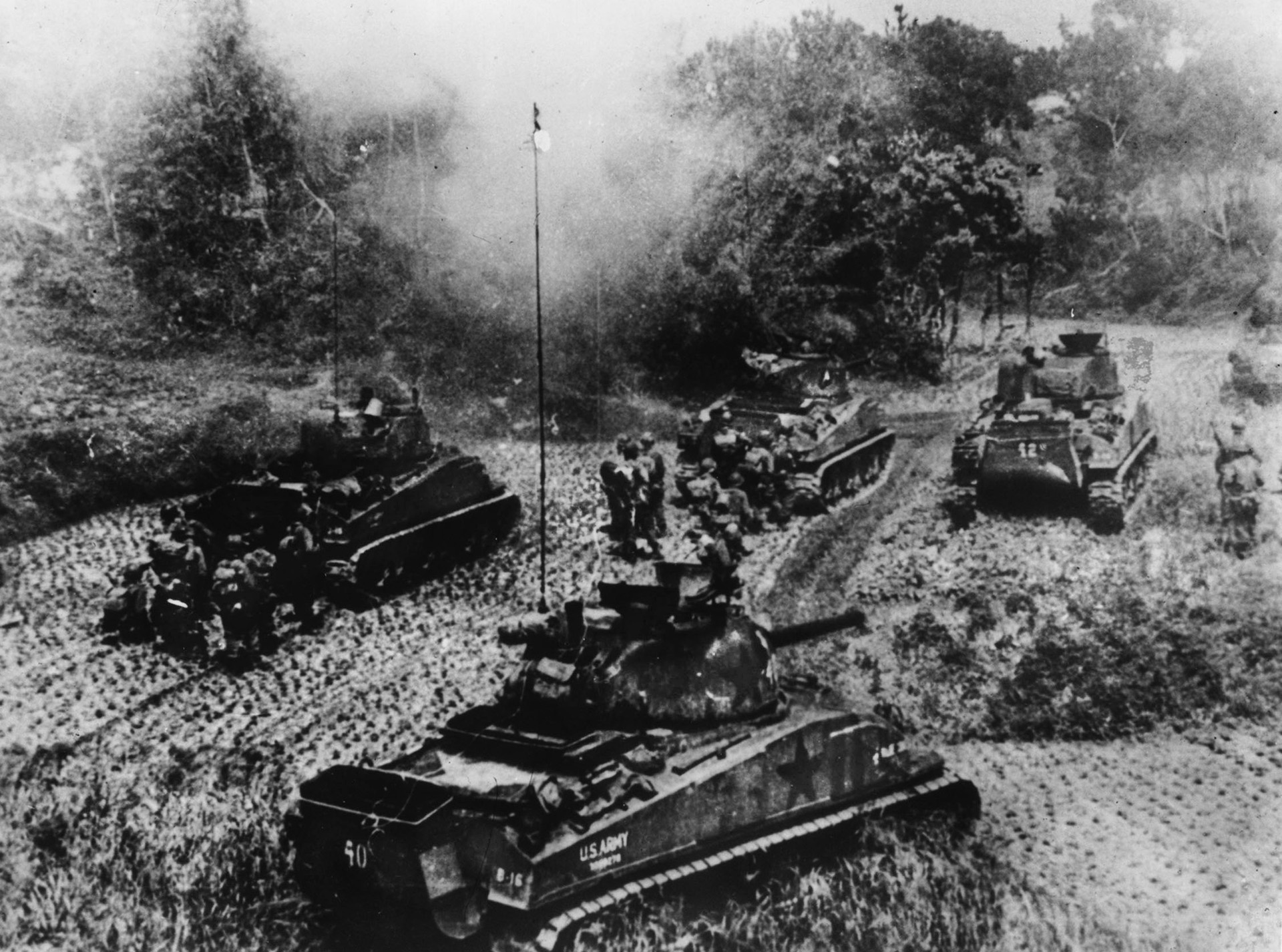 A quartet of American tanks, accompanied by infantrymen, advance against Japanese positions.