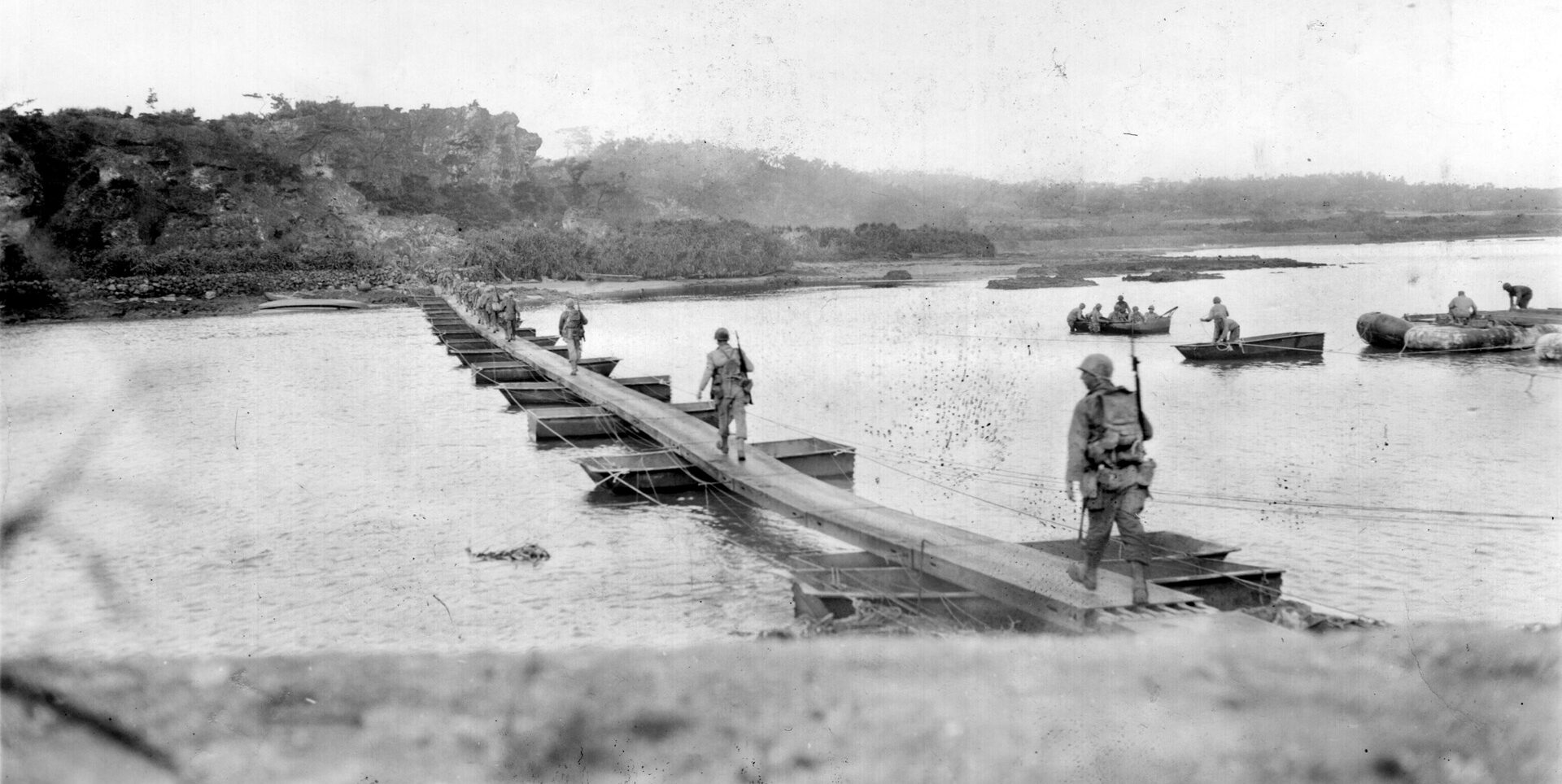 Men of the 27th Infantry Division’s Company A, 106th Infantry Regiment, cross a footbridge on their way to attack the Japanese in Machinato Village on April 18, 1945.